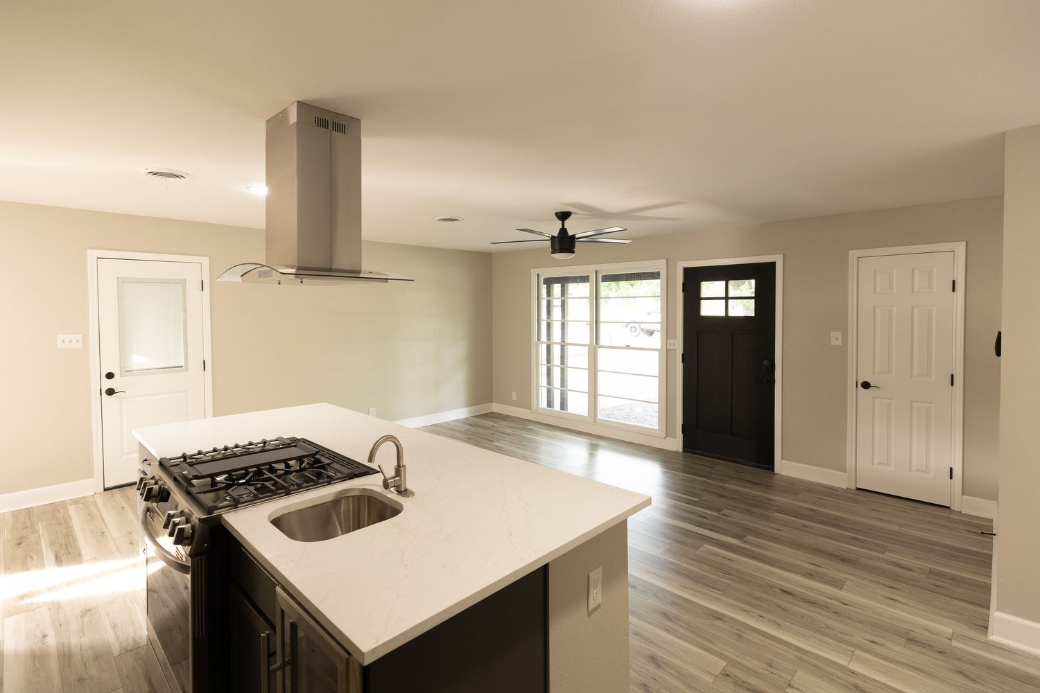 Modern kitchen island with gas cooktop, sink, and range hood, open to living area with hardwood floors and ceiling fan.
