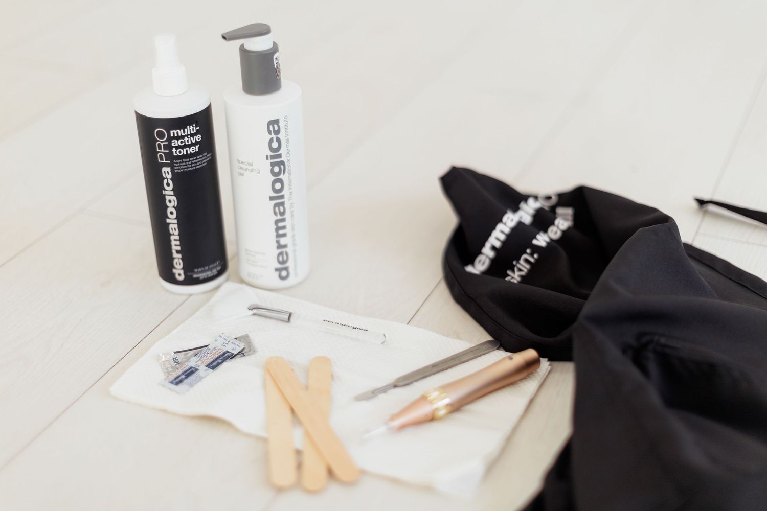 Dermalogica skincare products with applicator sticks, tweezers, and a black bag on a white surface.