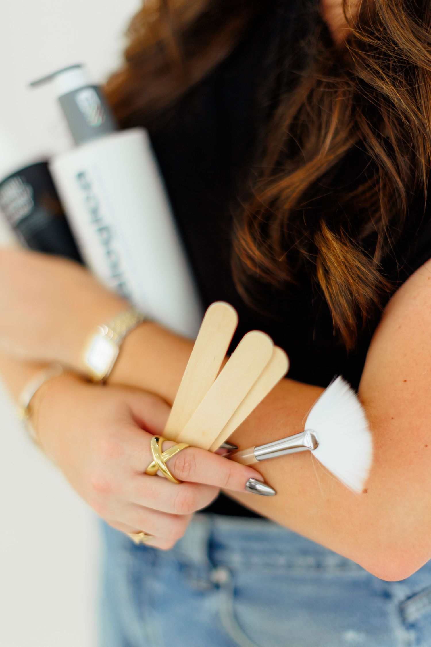 Woman holding wooden sticks and beauty tools with gold rings and bracelets visible.