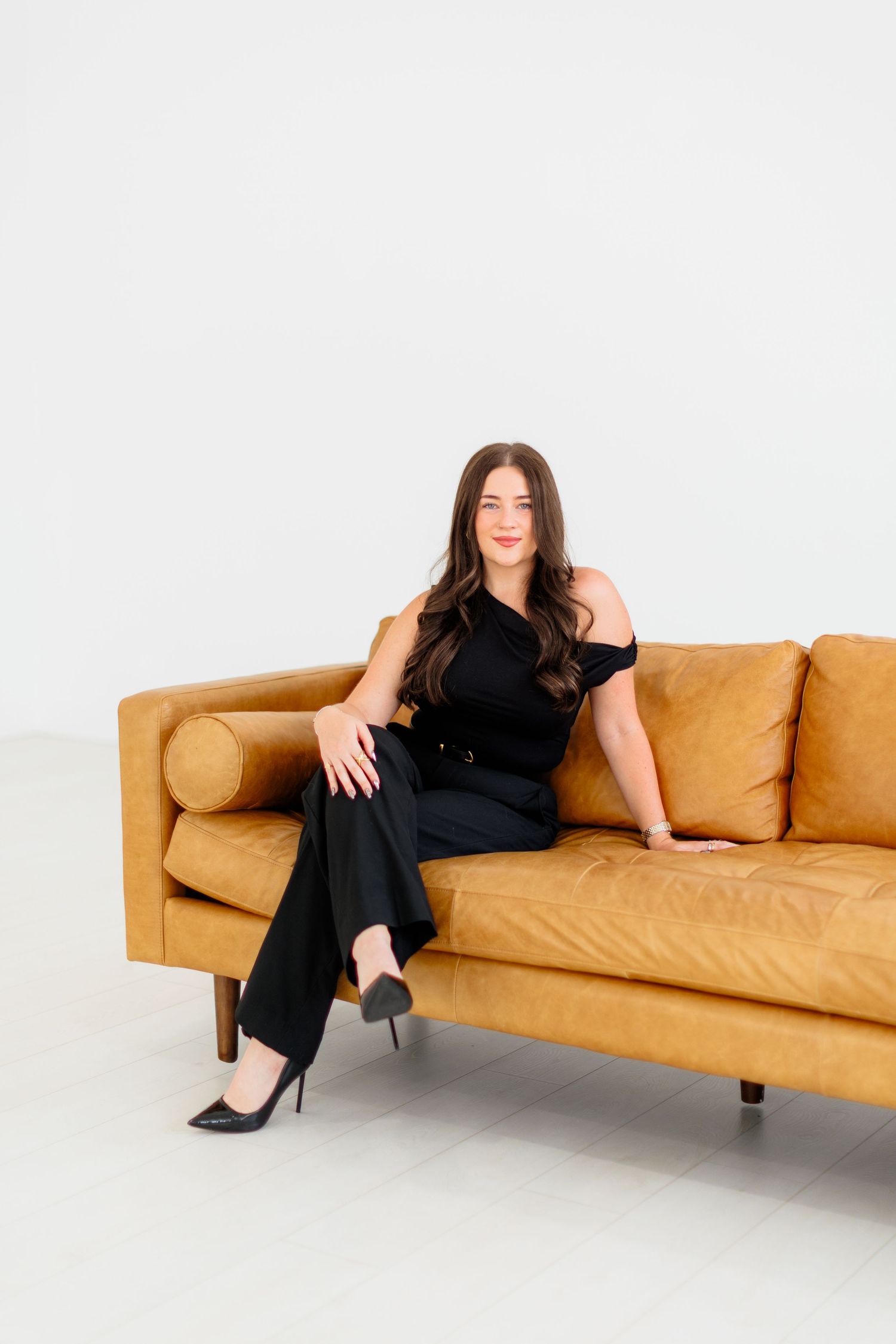 Woman in black outfit sitting relaxed on a tan leather sofa.