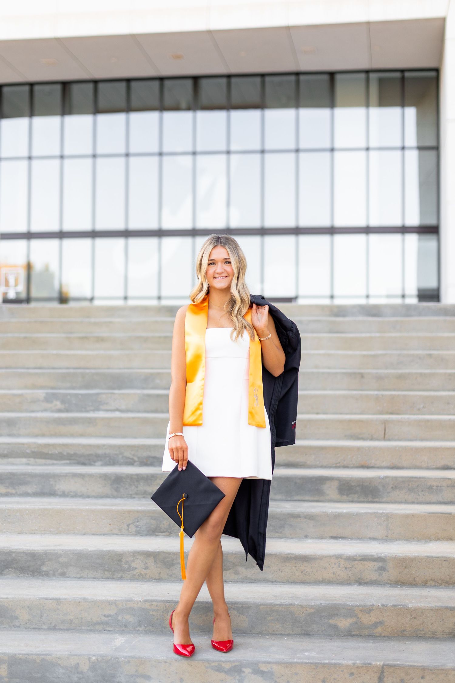 A series of graduation photos showing someone in a white dress and orange stole sitting on concrete steps with red heels.