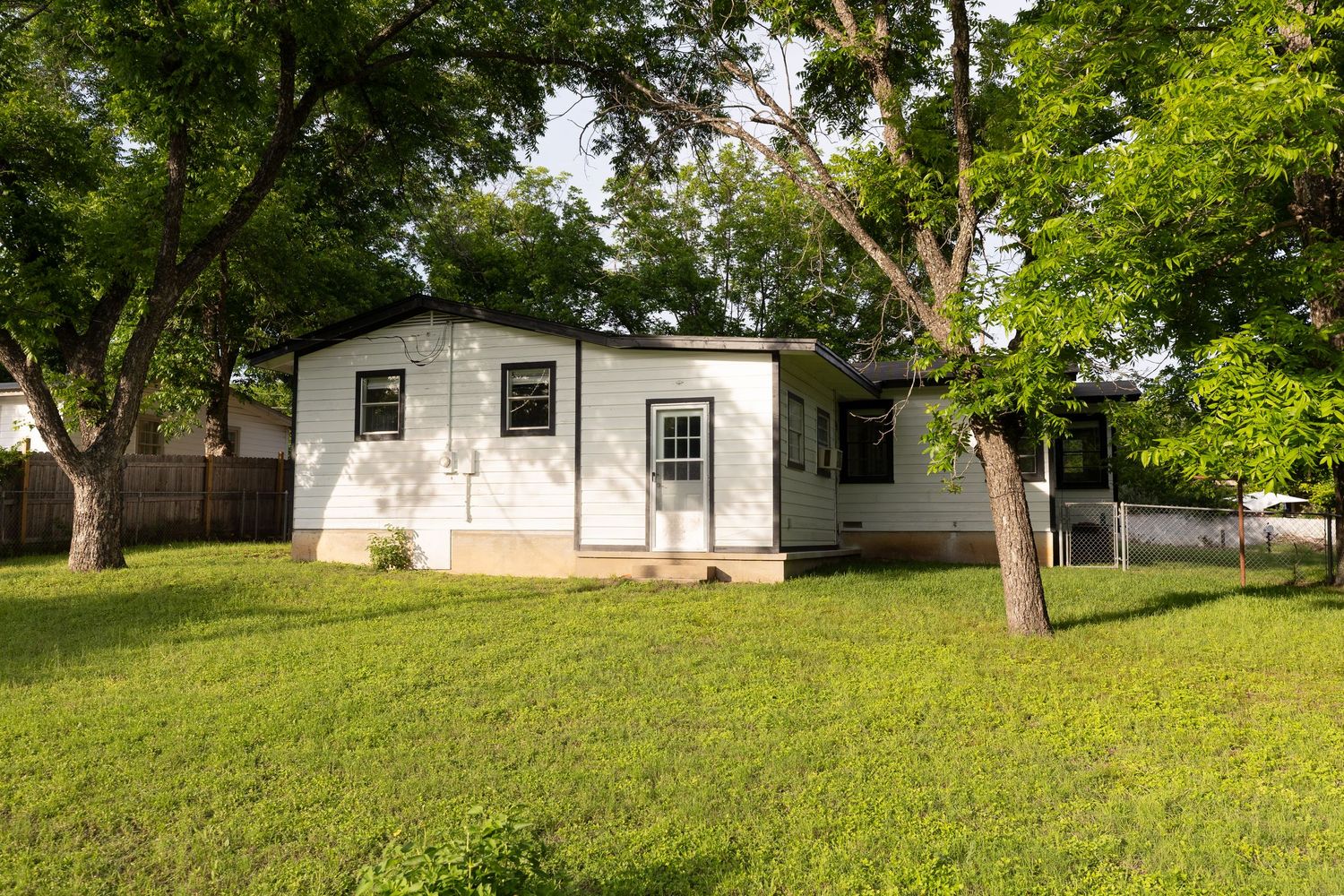 White single-story home with large shade trees, green lawn, and covered porch in a residential neighborhood.