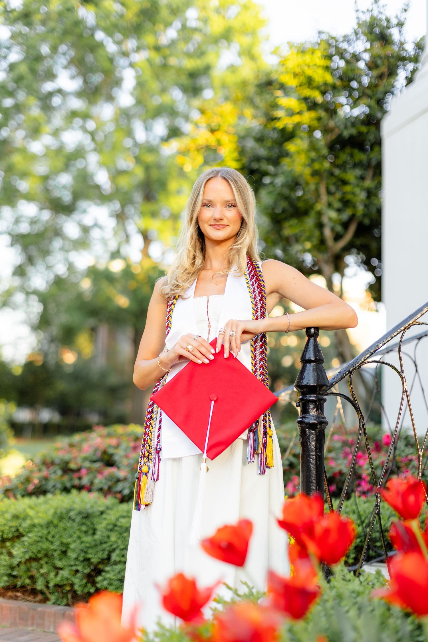 A person in a white dress poses in a garden with vibrant red poppies and yellow flowers in the background.