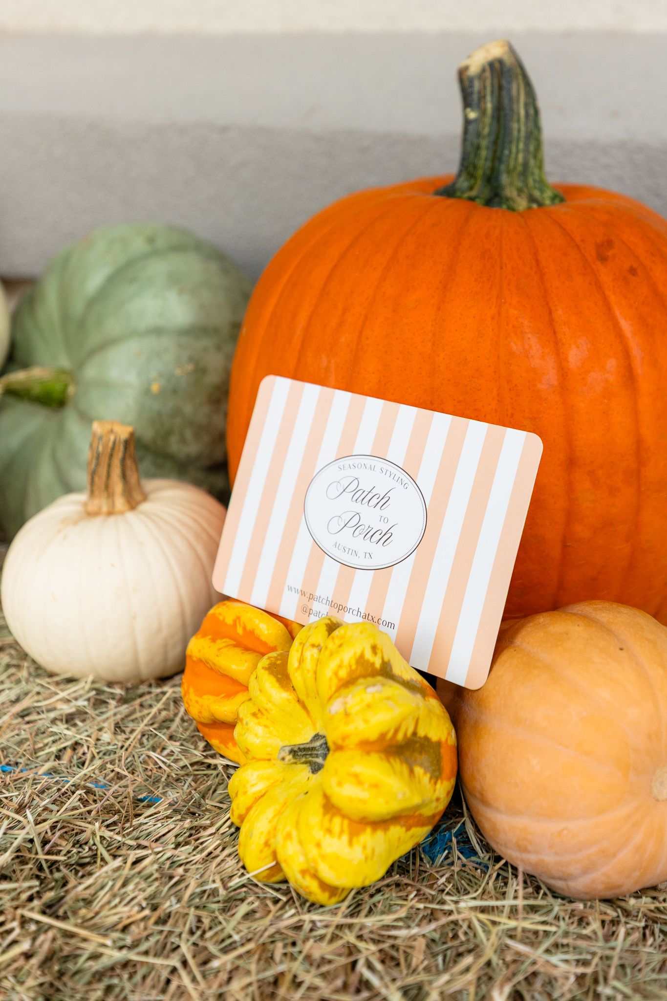 Orange and white pumpkins arranged on hay with small peach-colored place cards and yellow floral accents create a rustic display.