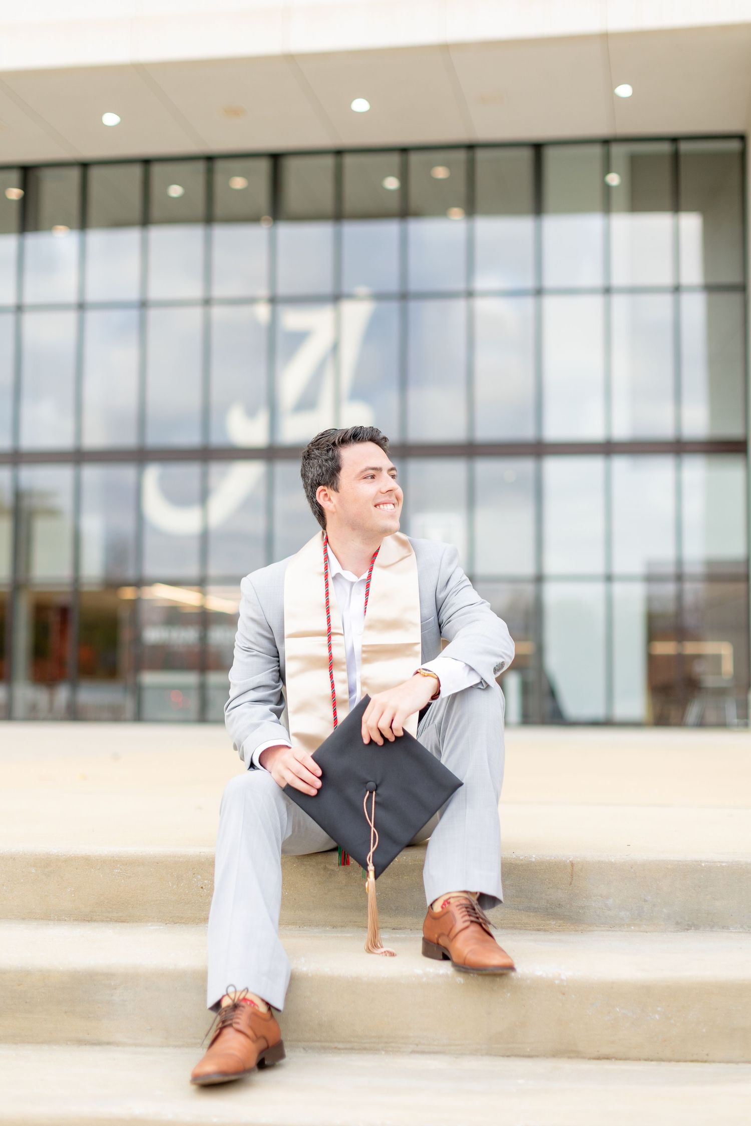 A person in a light gray suit sits casually on a concrete ledge in front of modern glass windows.