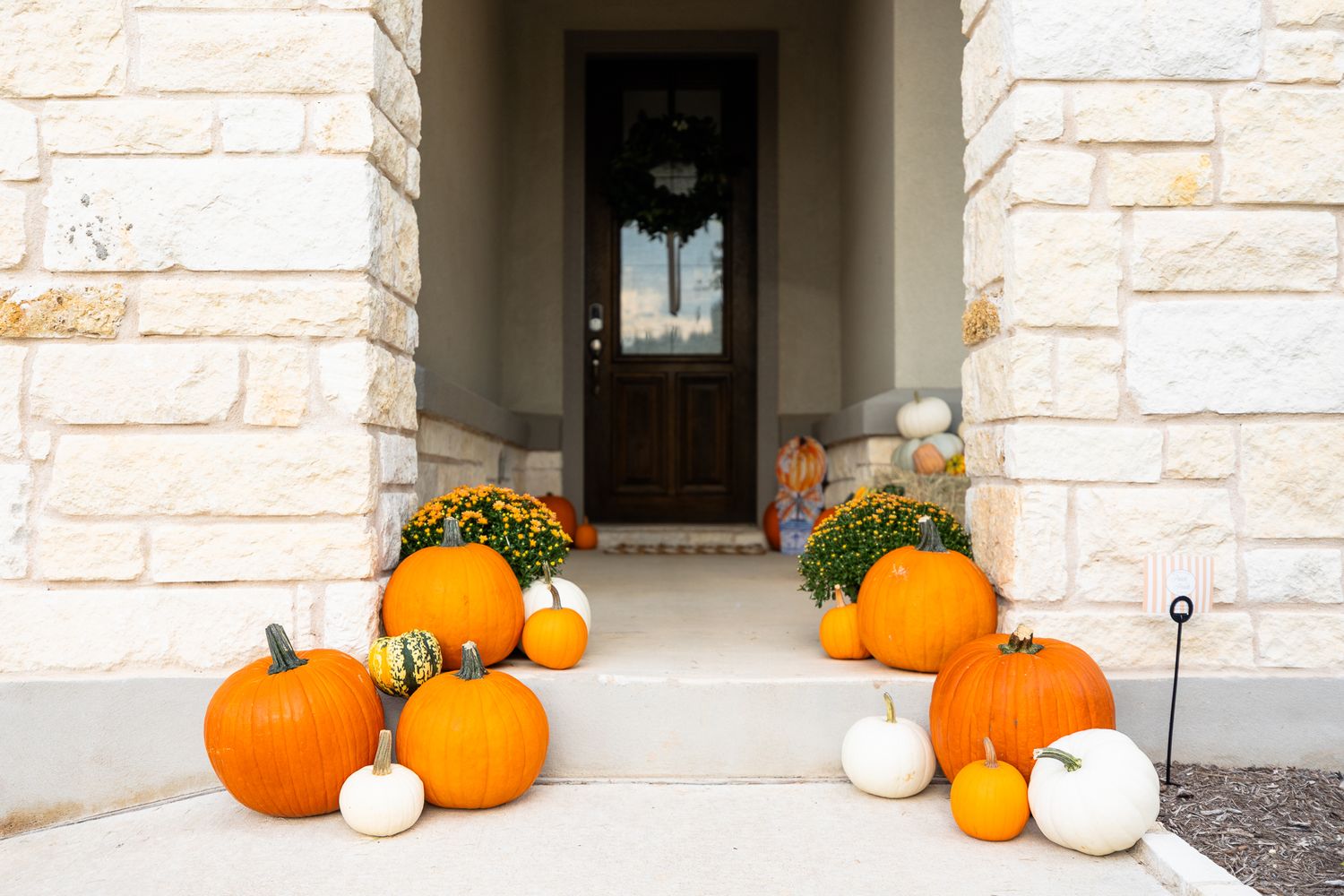 A row of decorative orange pumpkins and white gourds line a stone entryway for fall seasonal decor.
