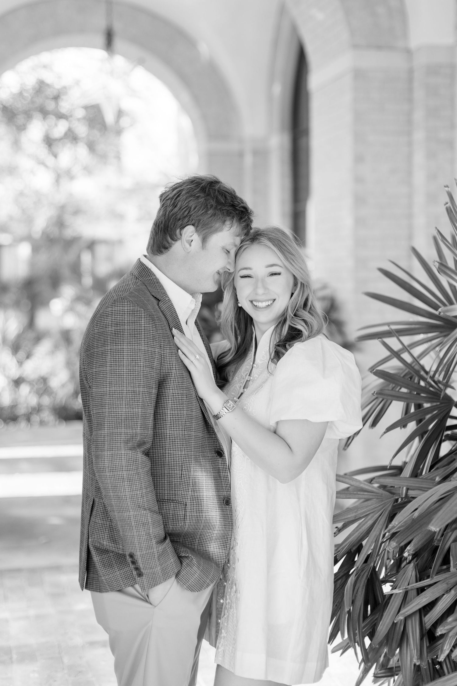 A couple shares intimate moments in black and white photos against a backdrop of tropical plants.