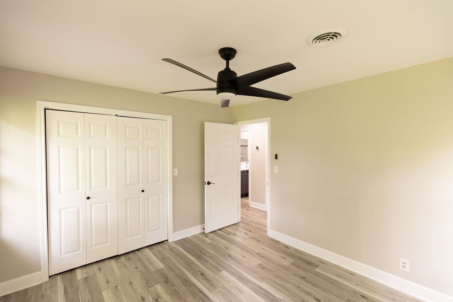 Empty bedroom with hardwood floors, white closet doors, and a modern black ceiling fan.