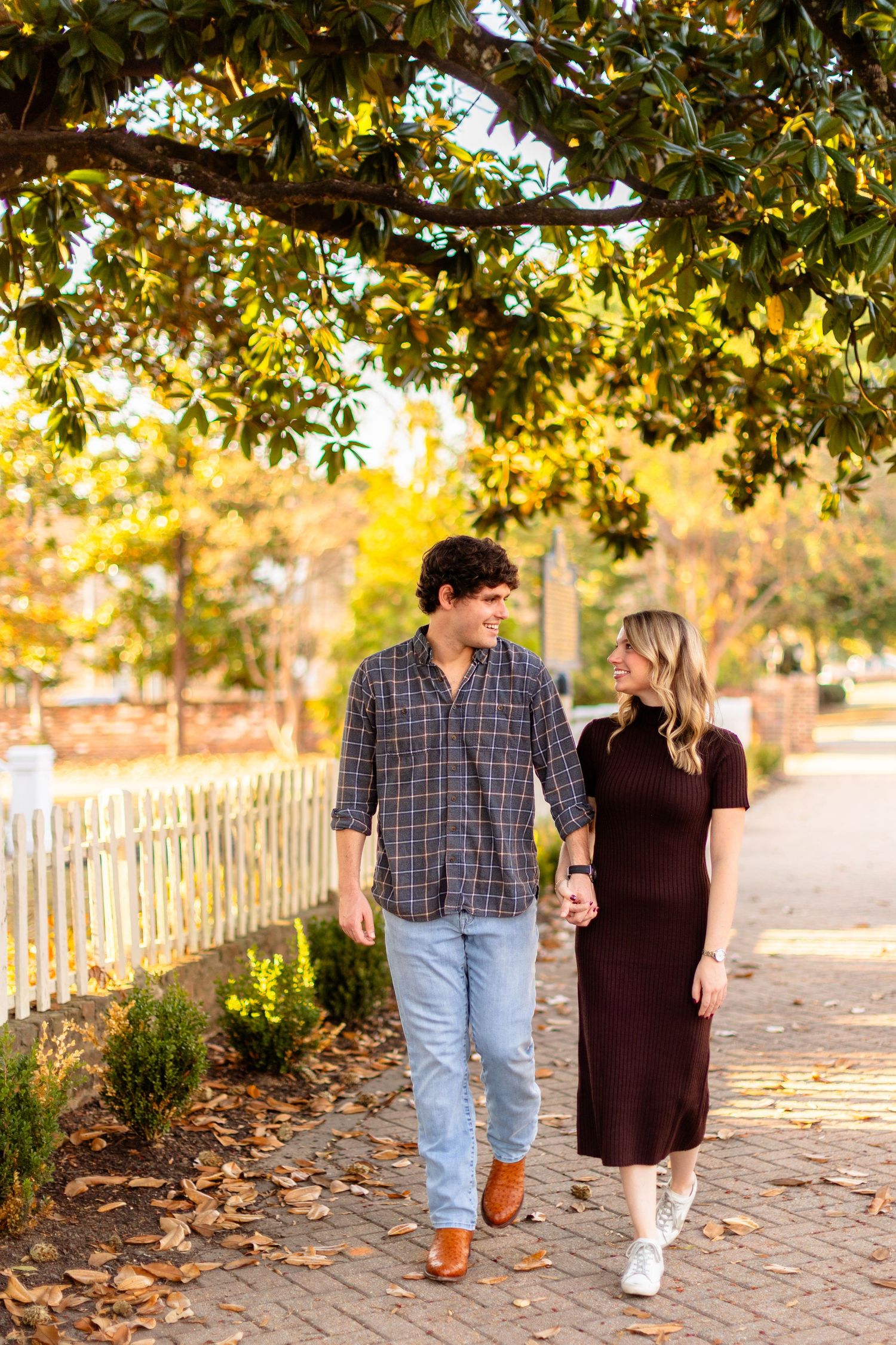 A couple walks together on a brick path under autumn trees with golden sunlight filtering through the leaves.