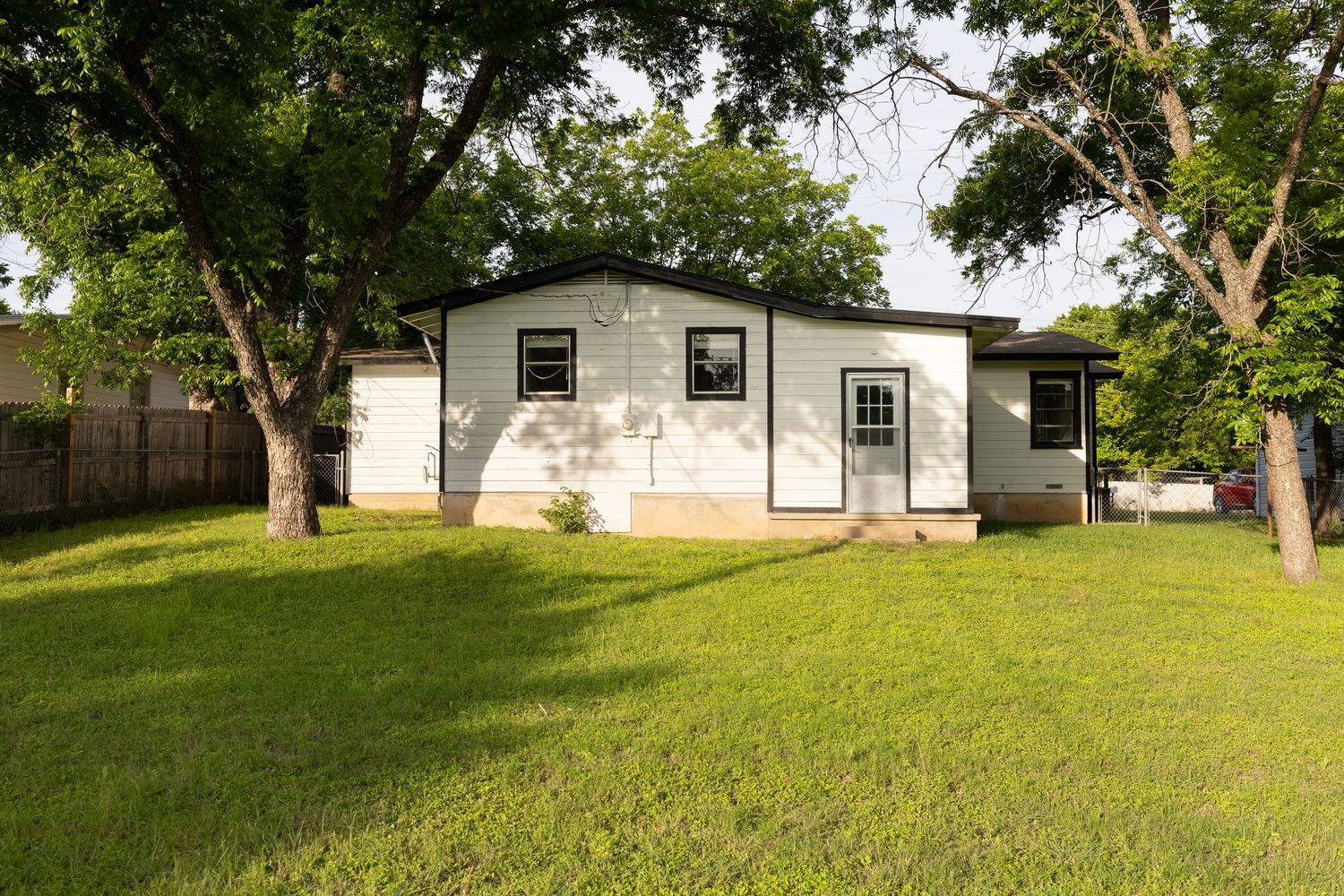 White ranch-style home with large green lawn and mature shade trees.