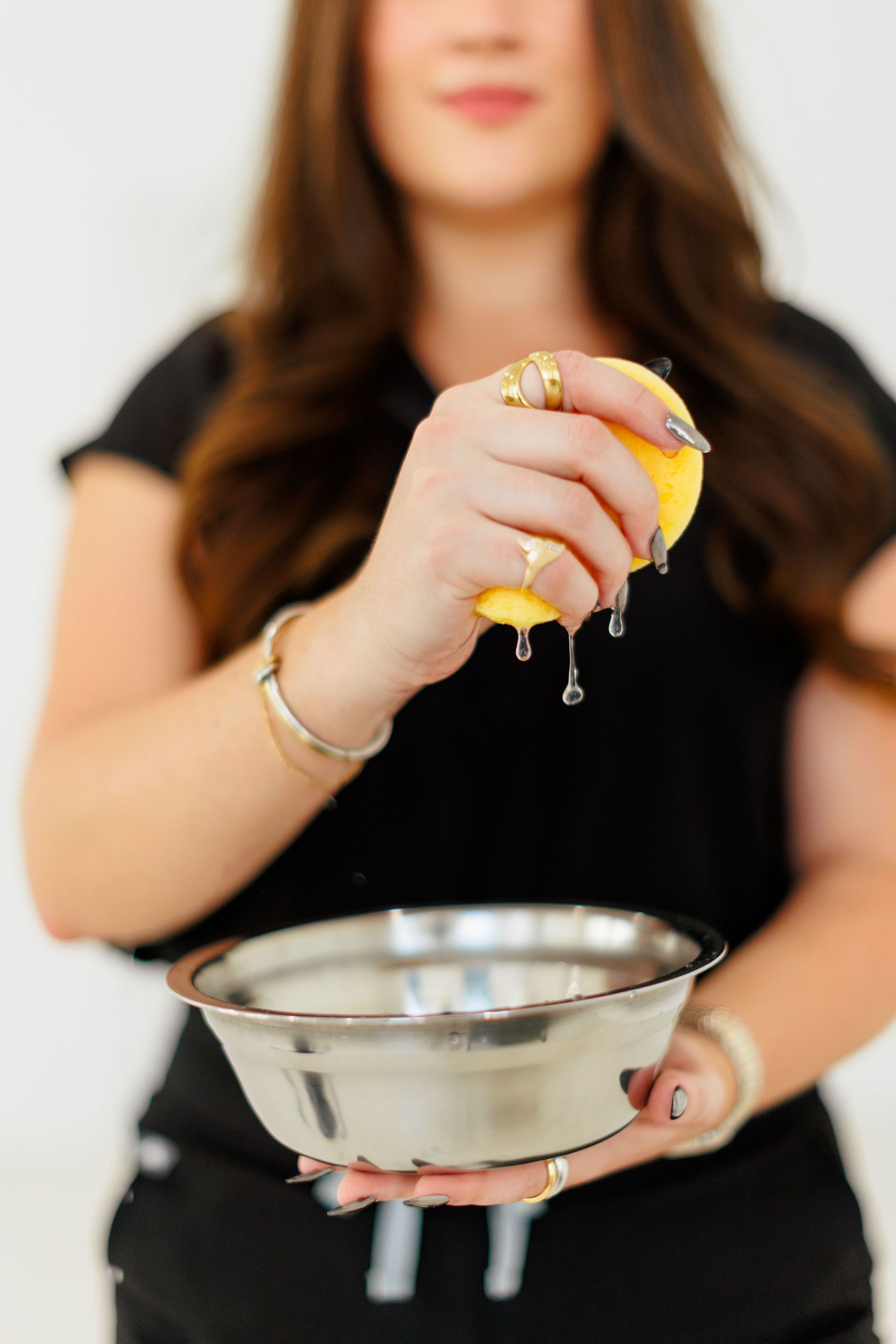 Woman squeezing fresh lemon juice into a stainless steel bowl, wearing gold jewelry.