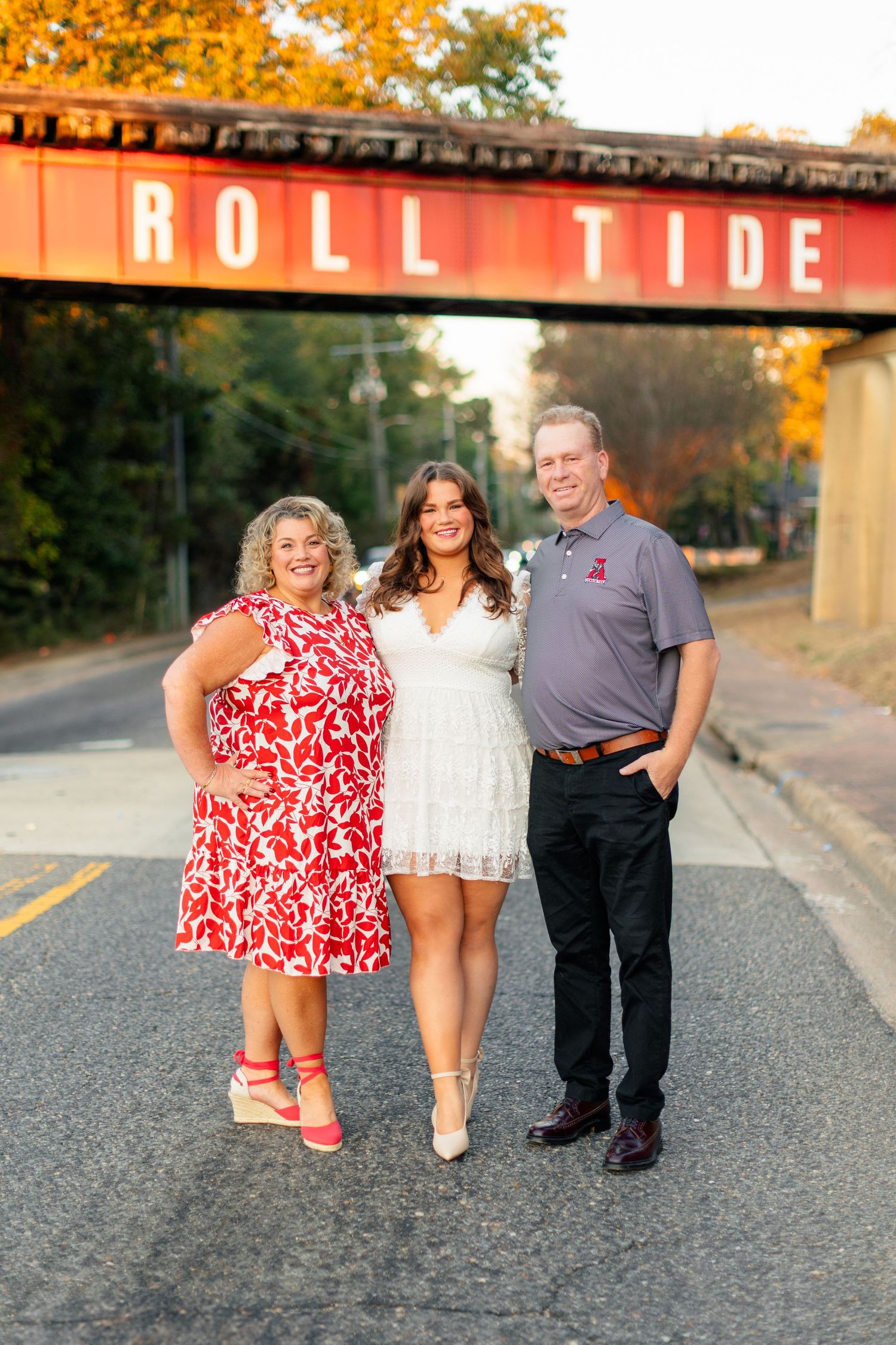 Three people pose playfully on a road at sunset with warm golden lighting and rustic buildings in the background.