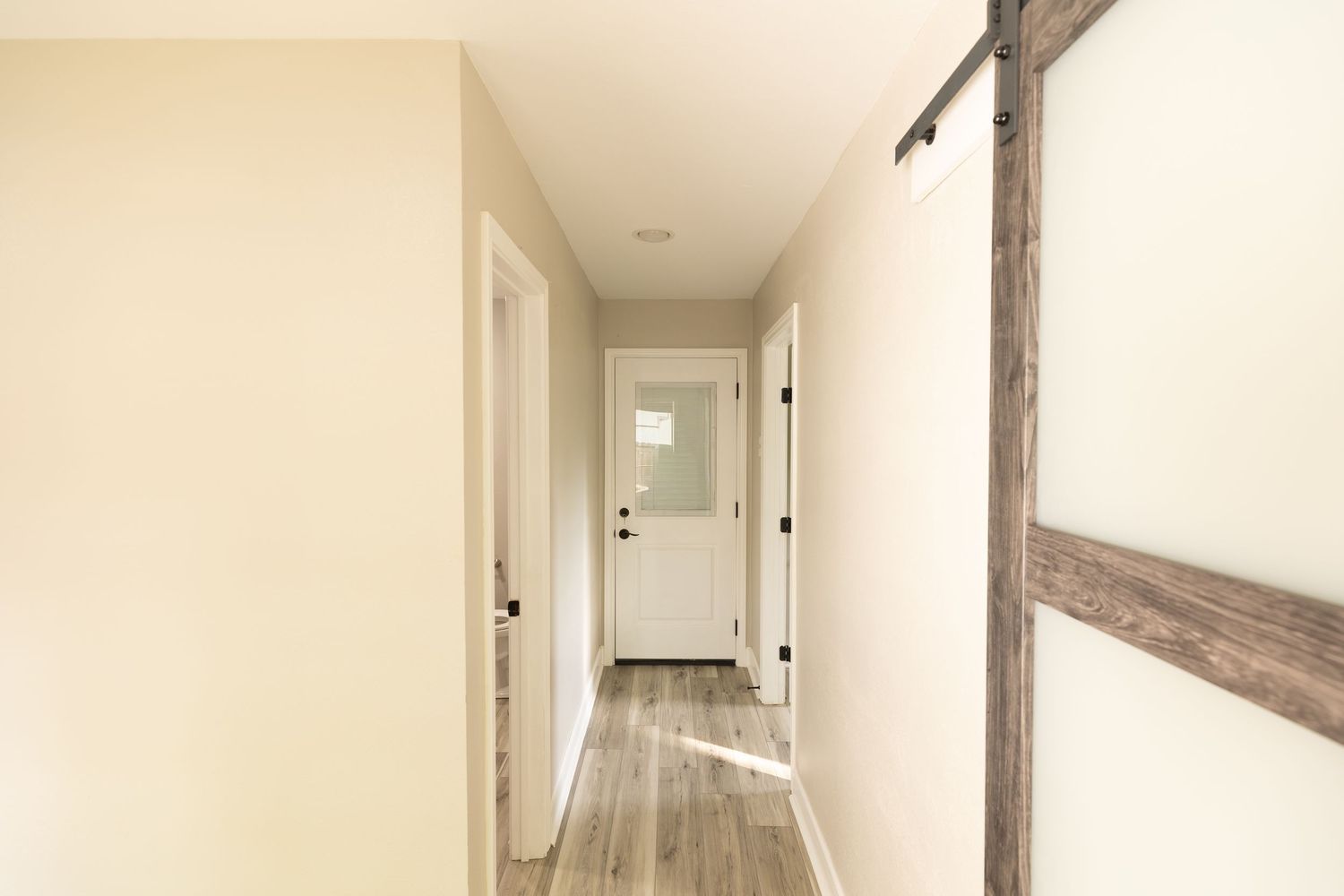 Bright hallway with light wood floors, white walls, and a rustic barn door leading to multiple rooms.