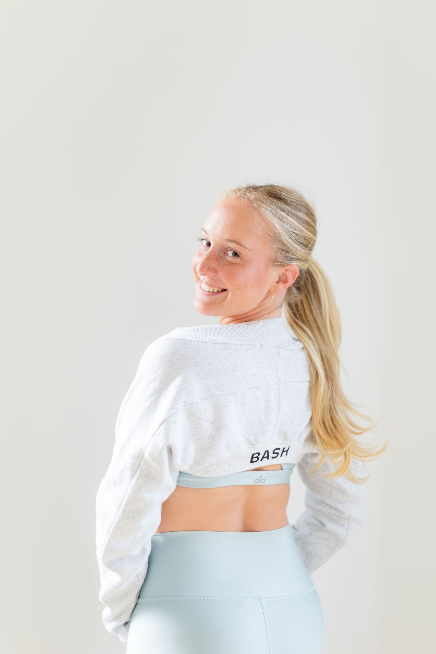 Person wearing white crop sweatshirt and light blue leggings looking over shoulder.