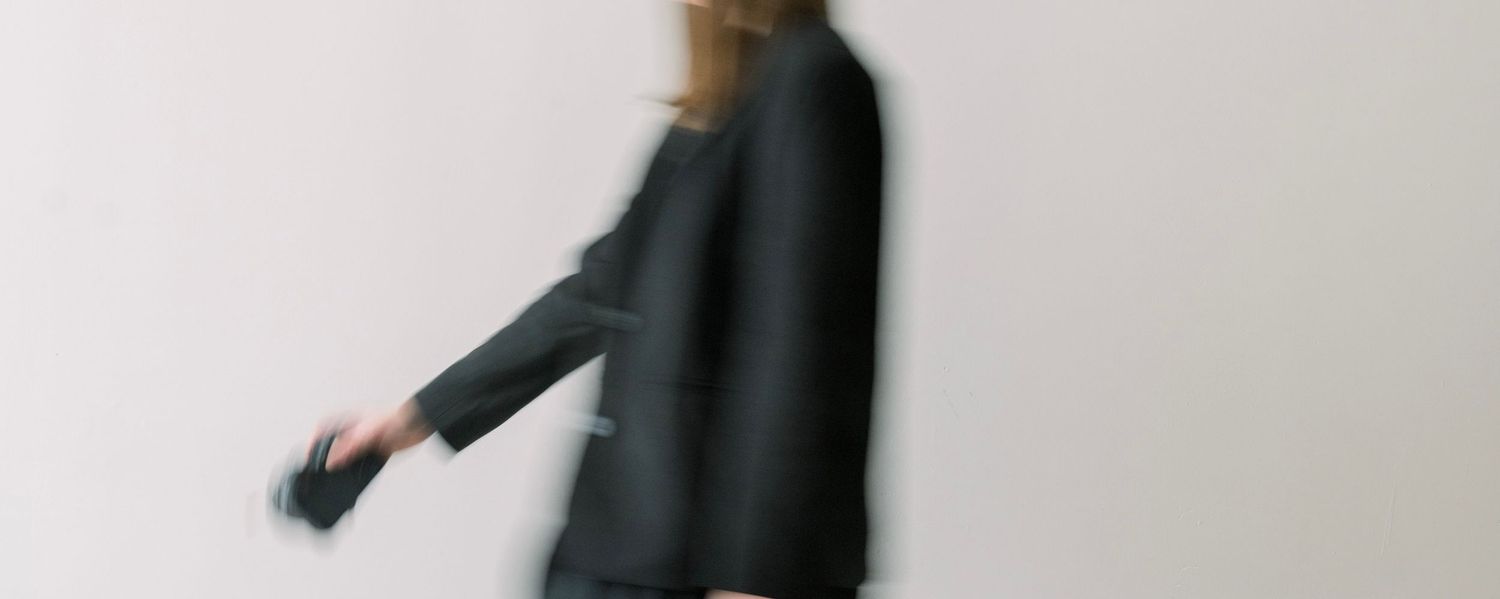 Blurred motion shot of person in black clothing walking against white wall.