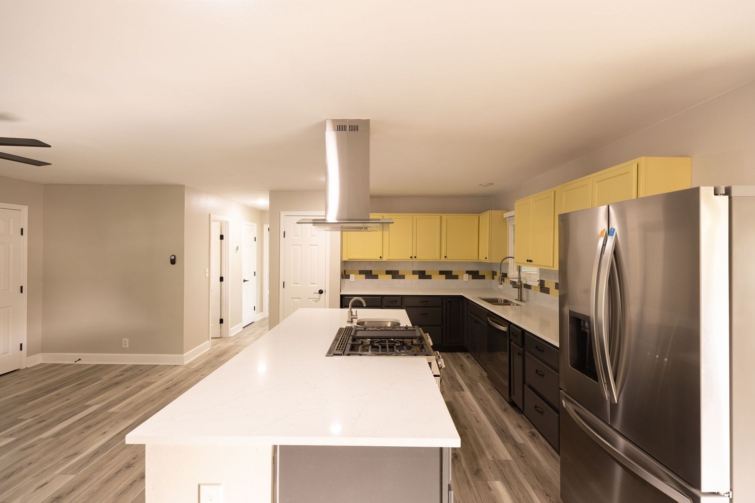 Modern kitchen with yellow cabinets, stainless steel appliances, island with white countertop, and hardwood floors.