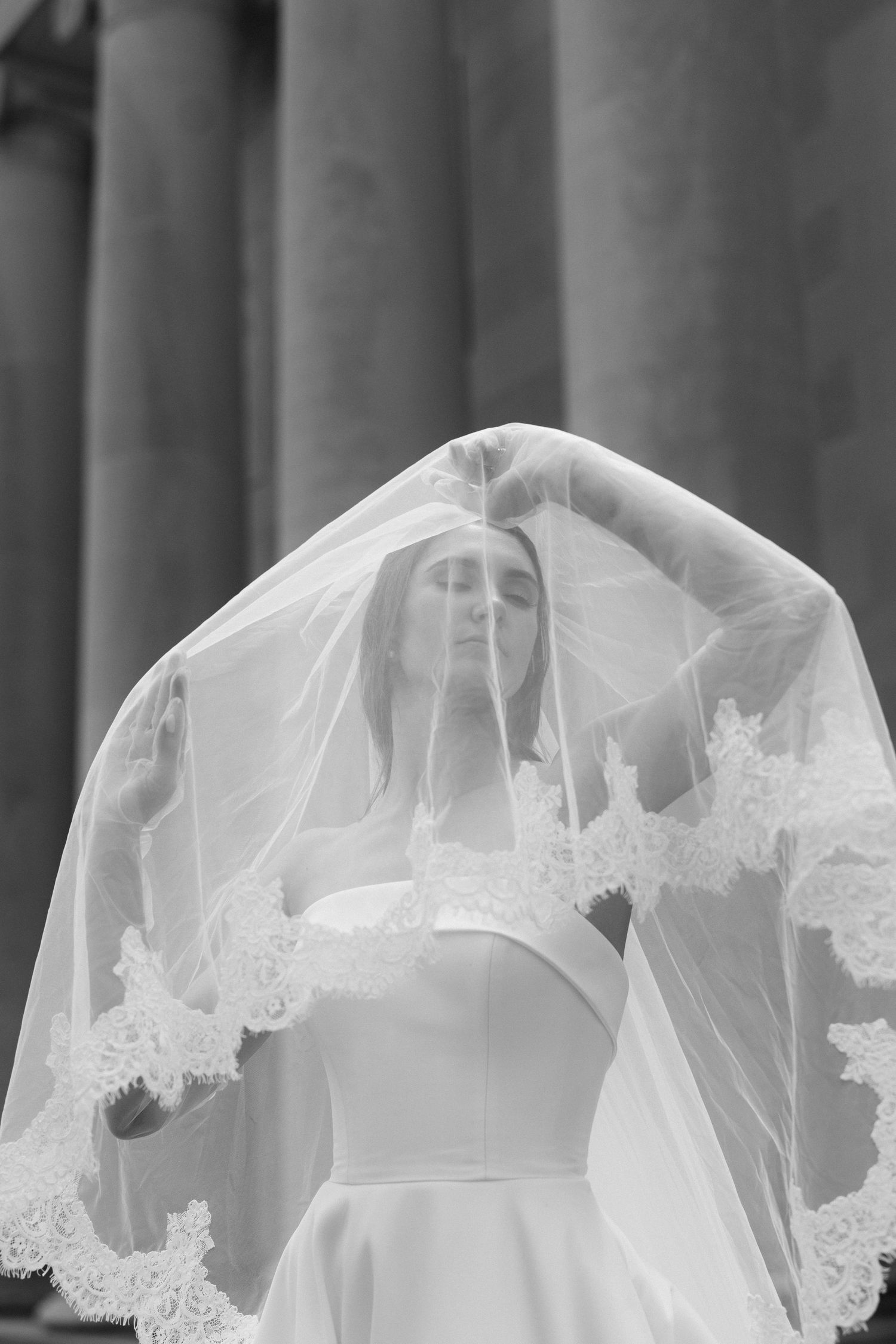Close-up of delicate white lace veil with floral details flowing in gentle breeze against blurred backdrop.