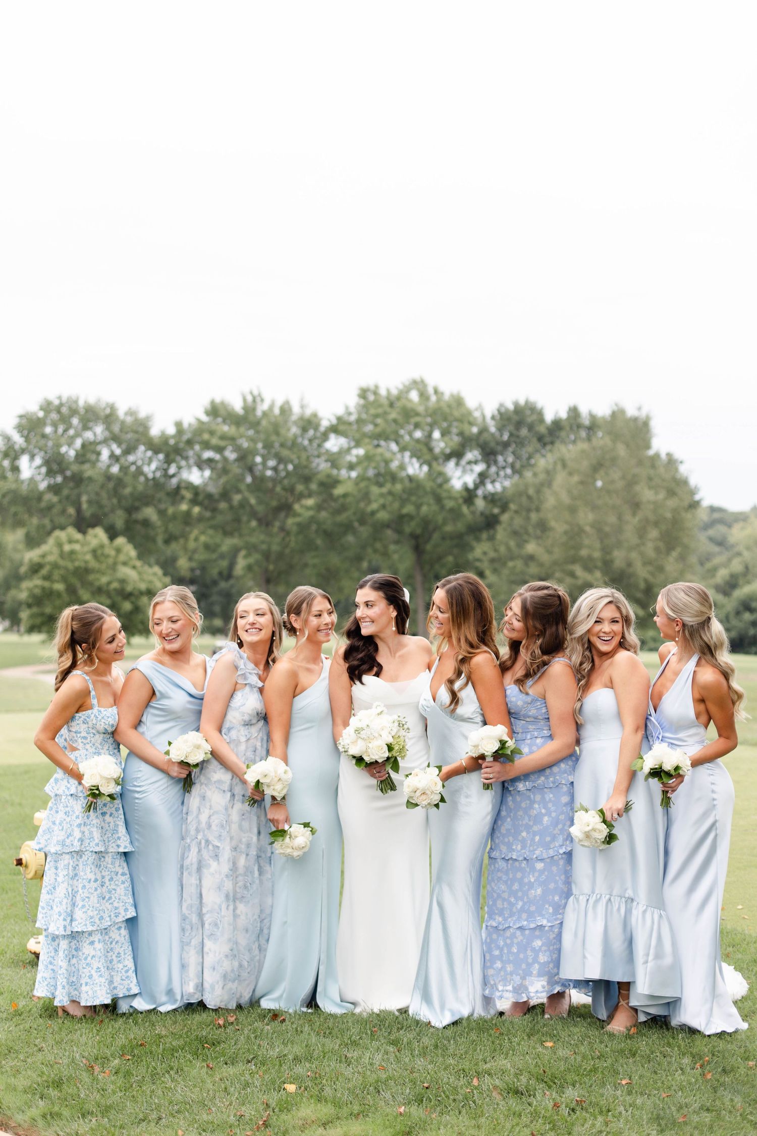 Bridesmaids in light blue dresses standing together on a grassy lawn with bouquets at Mission Hills Country Club Wedding in Kansas City.