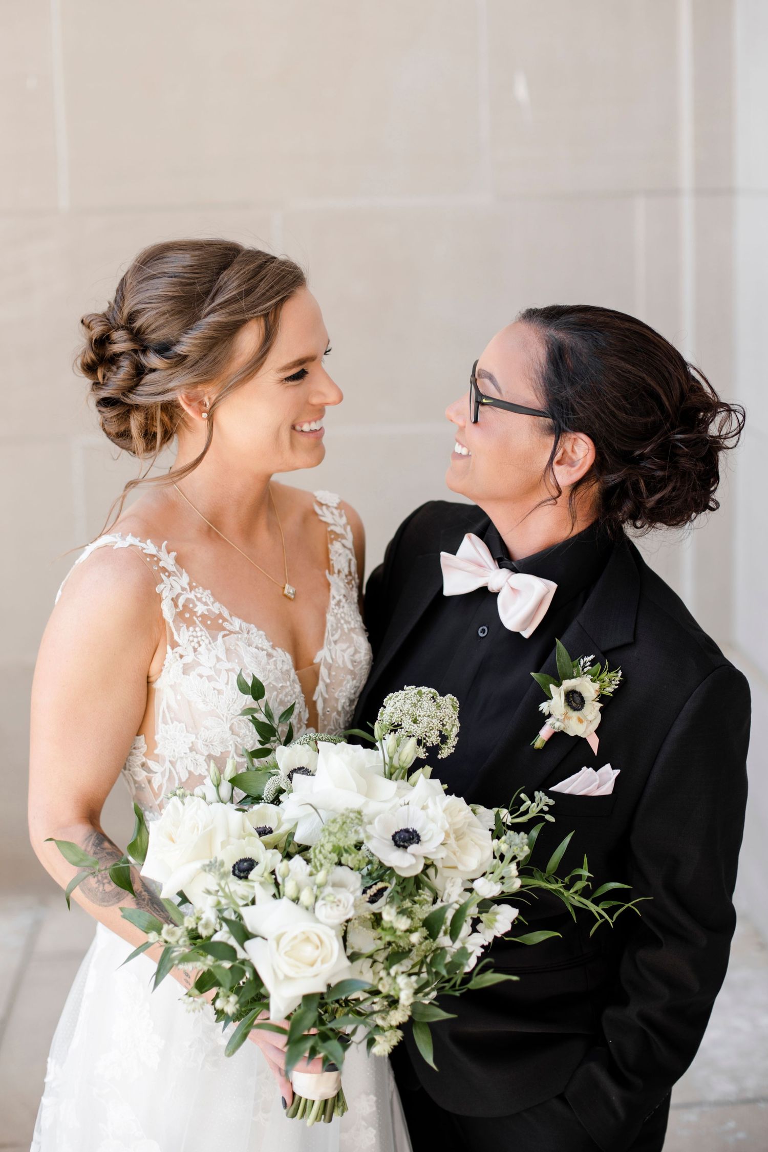 A happy wedding couple in formalwear shares a tender moment while holding a white and green floral bouquet.