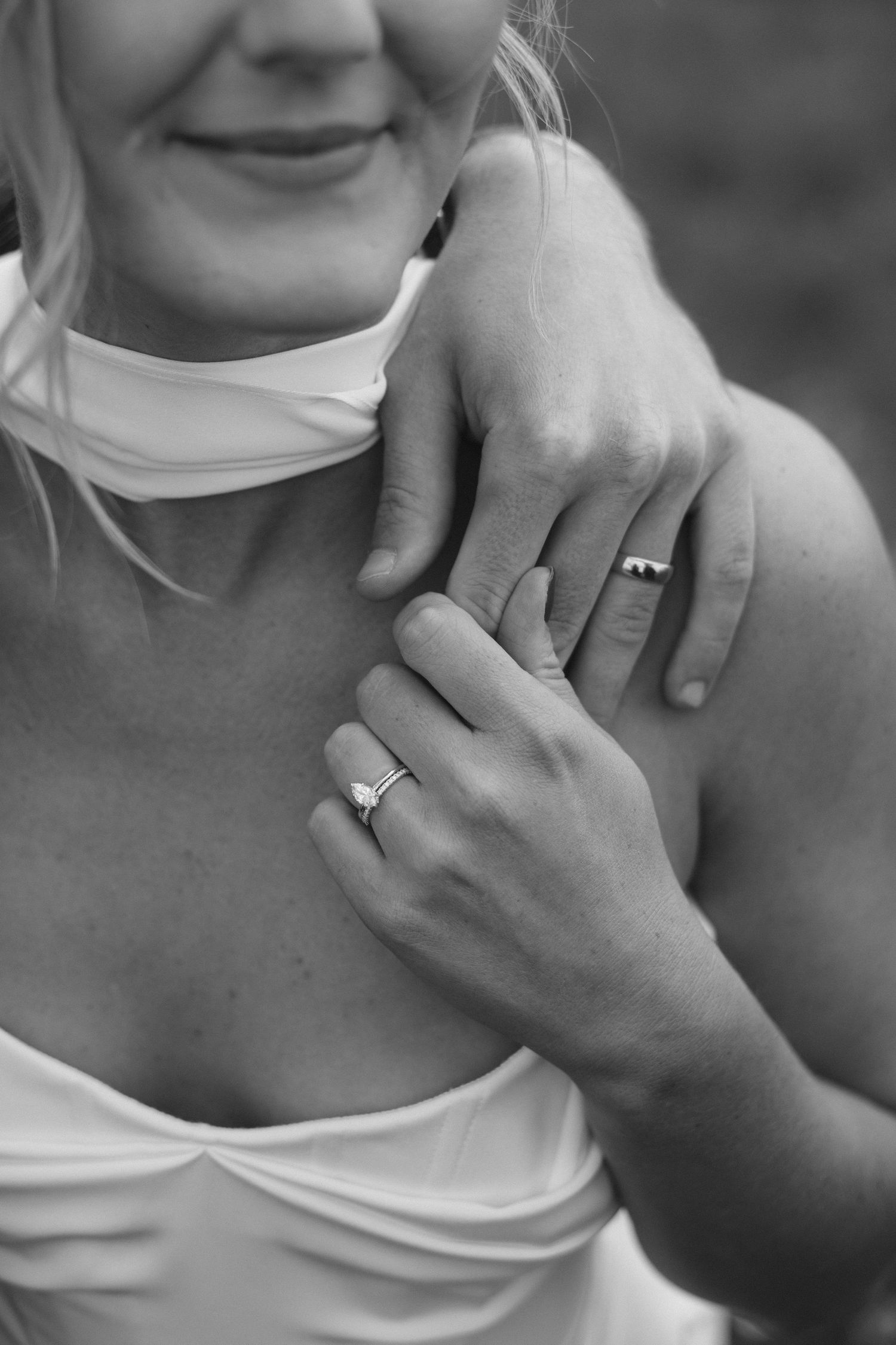 Black and white close up of hands wearing engagement rings against white fabric with a romantic feel.
