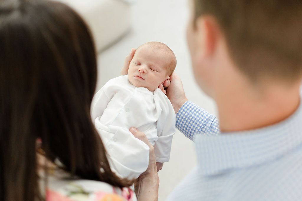 A sleeping newborn baby dressed in white is gently cradled during an intimate family moment. Kansas City Newborn Photographer Hannah Taylor.