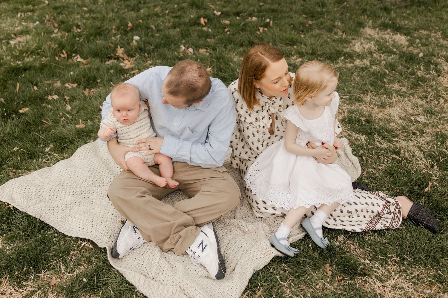 Family sits together on picnic blanket during outdoor lifestyle photo session in grassy field at golden hour.