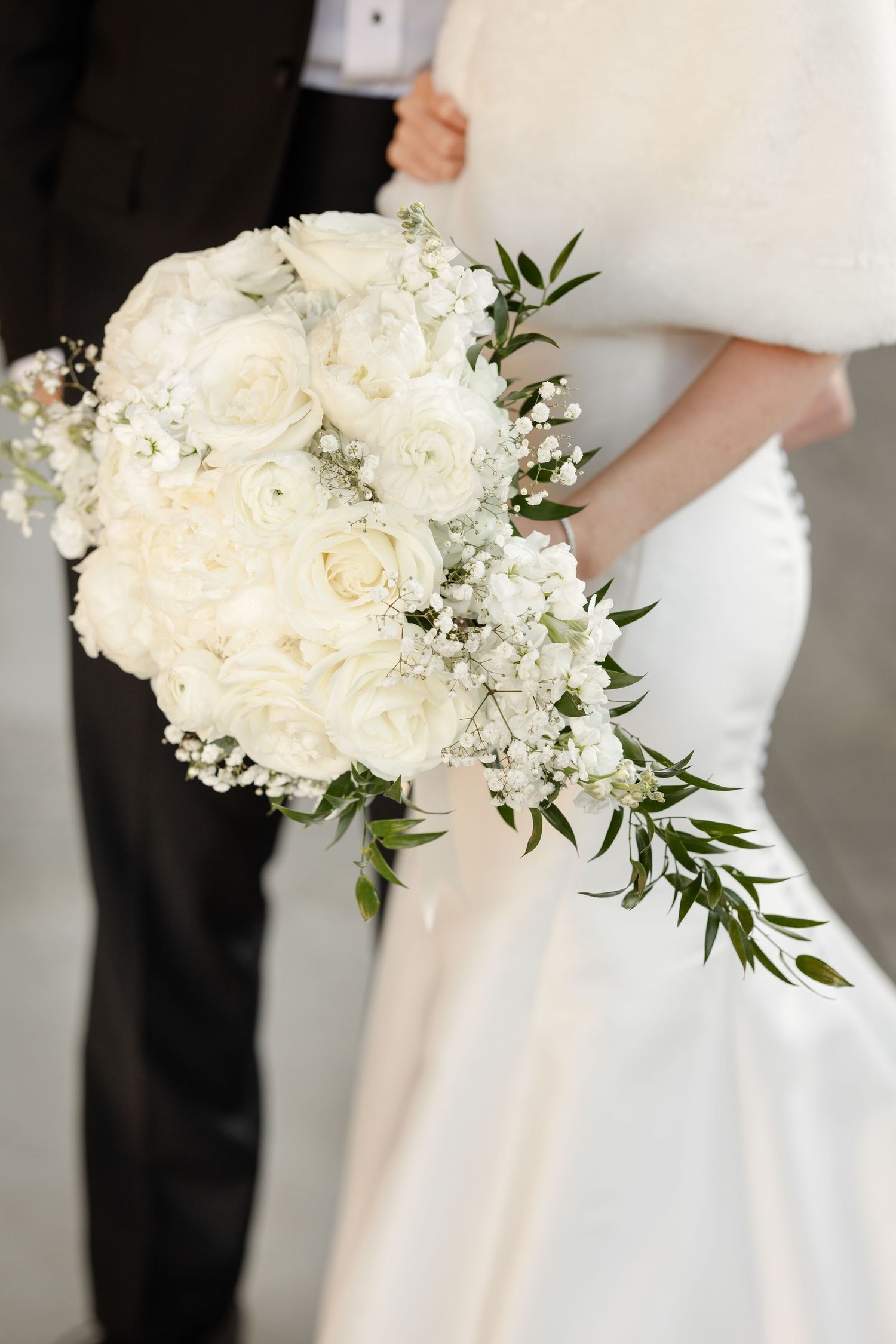 An elegant white bridal bouquet with roses, baby's breath and cascading greenery.