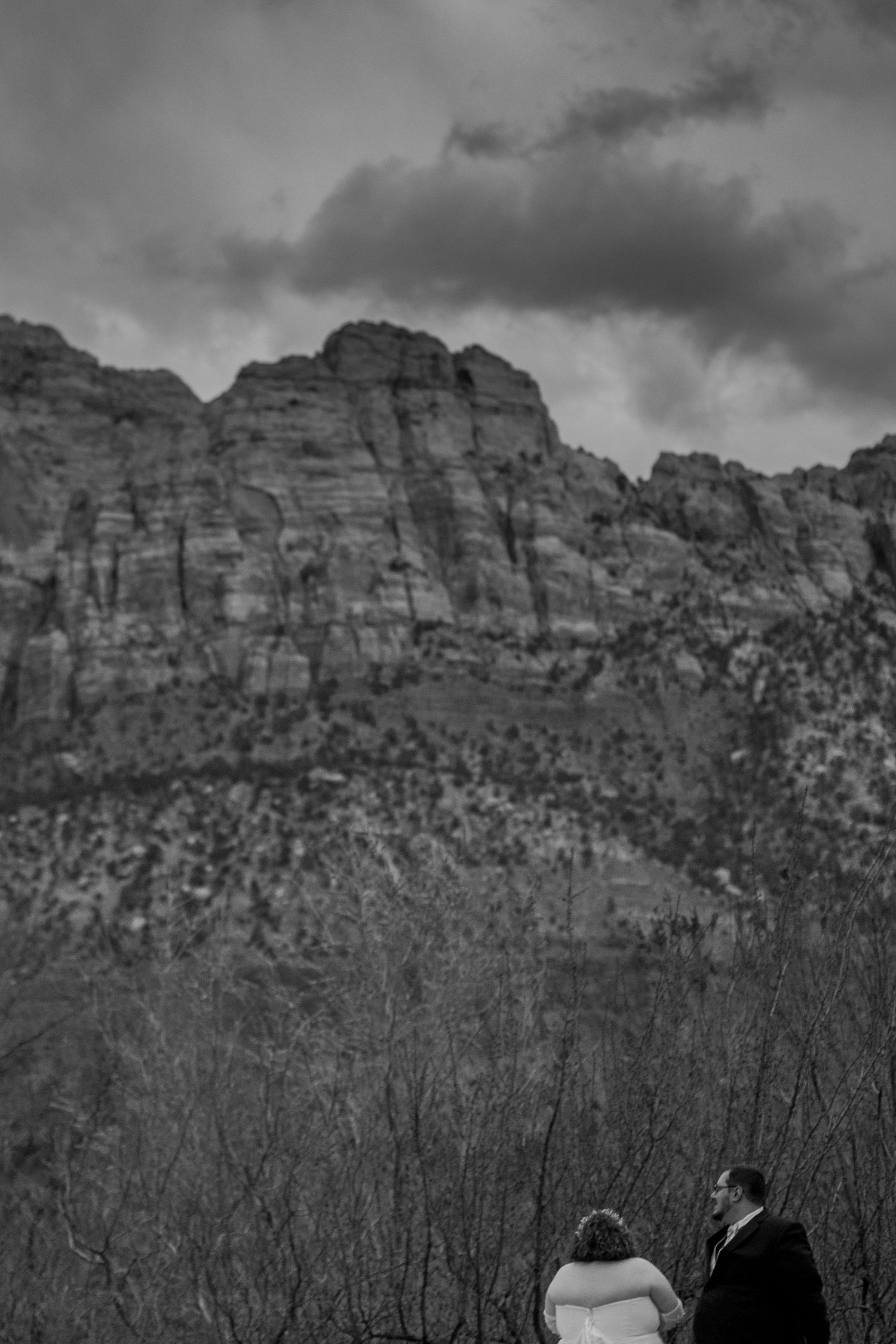 Wedding couple silhouetted against dramatic rocky mountain landscape in black and white at Zion National Park elopement.