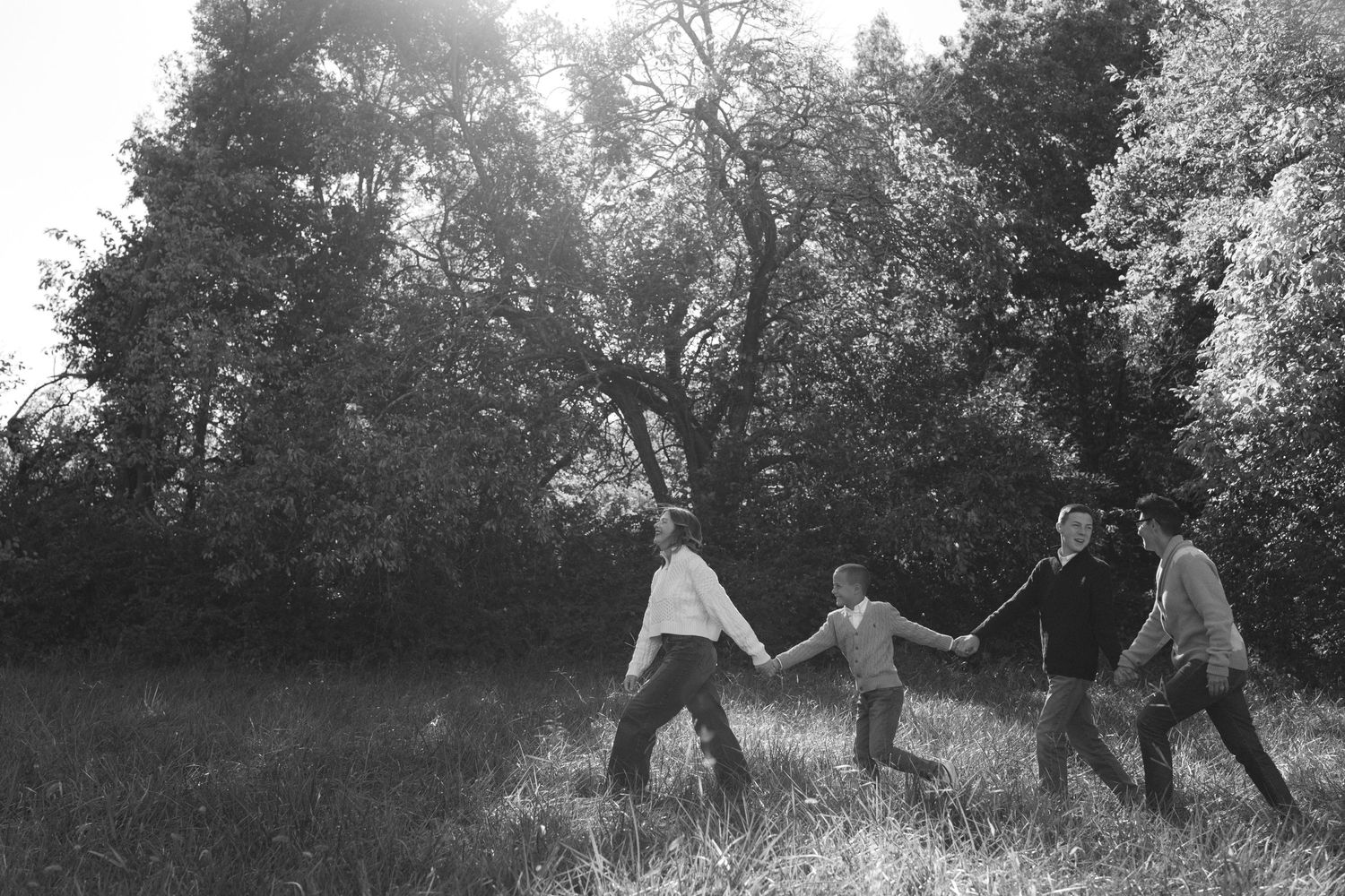 Black and white image of family holding hands while running through meadow at Shawnee Mission Park in Kansas City.