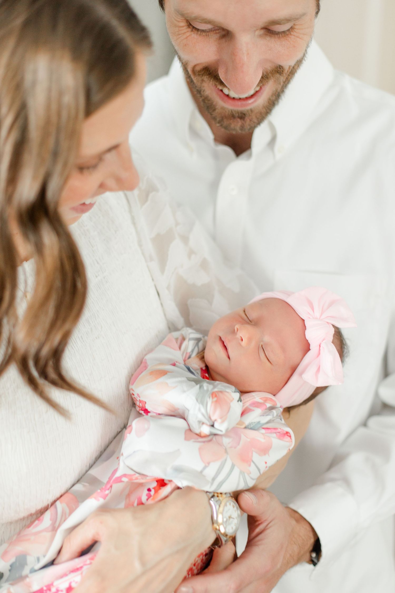Parents gazing lovingly at their newborn baby wearing a pink bow.