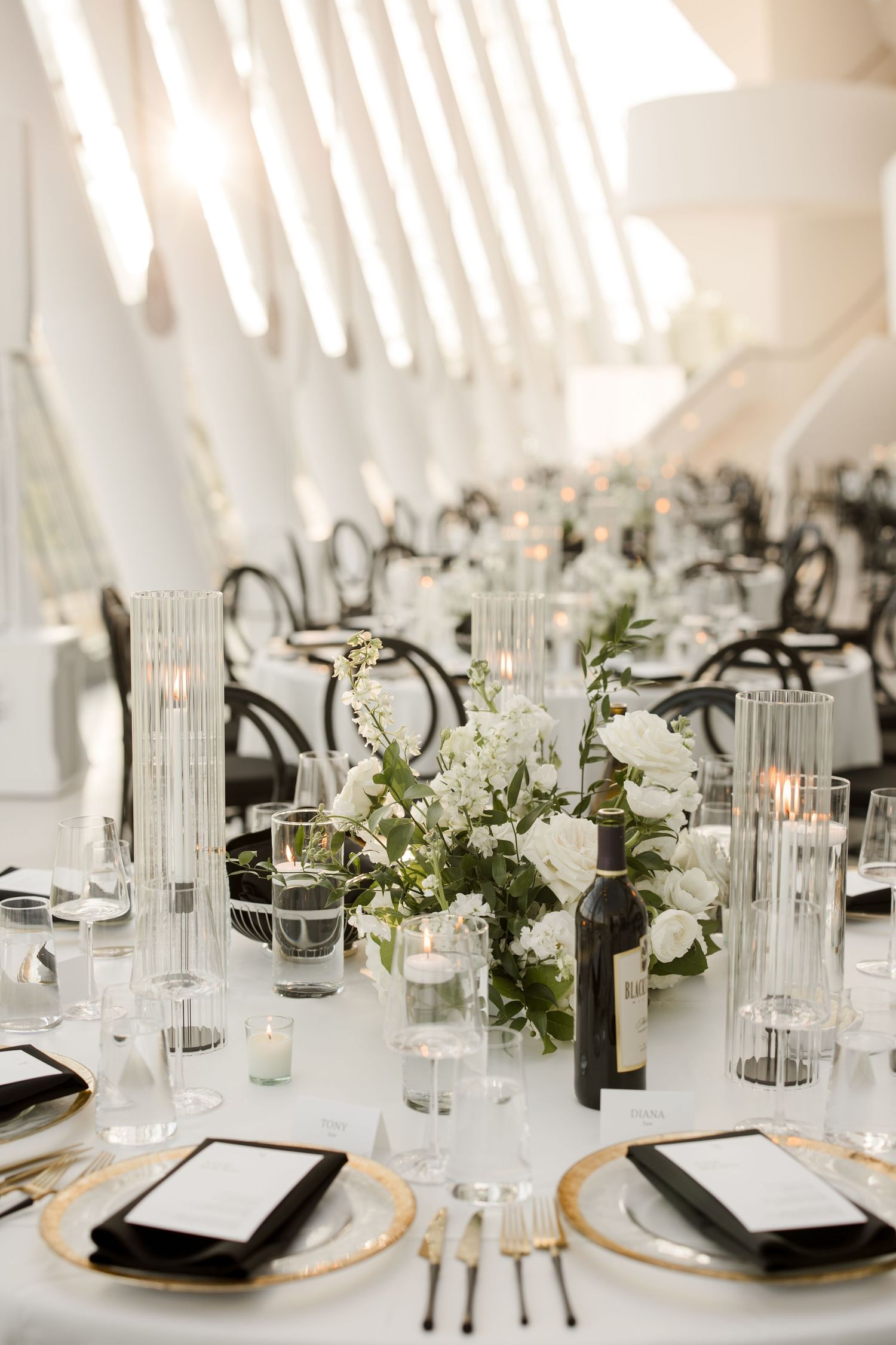 Elegant wedding table settings with white florals, glass candleholders, and gold charger plates.