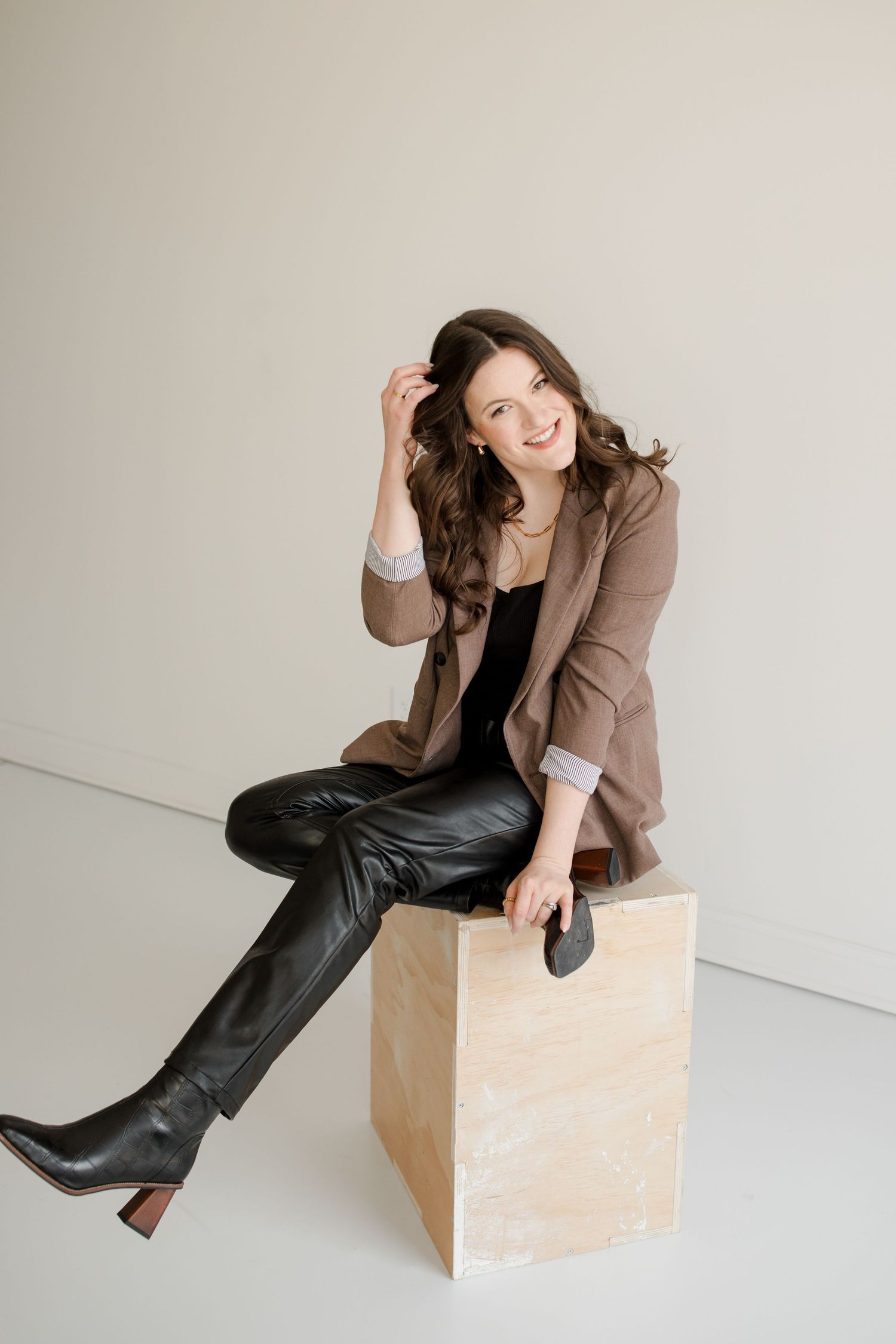 Casual portrait of person in brown blazer and leather pants sitting on geometric cube. KC Wedding Photographer Hannah Taylor.