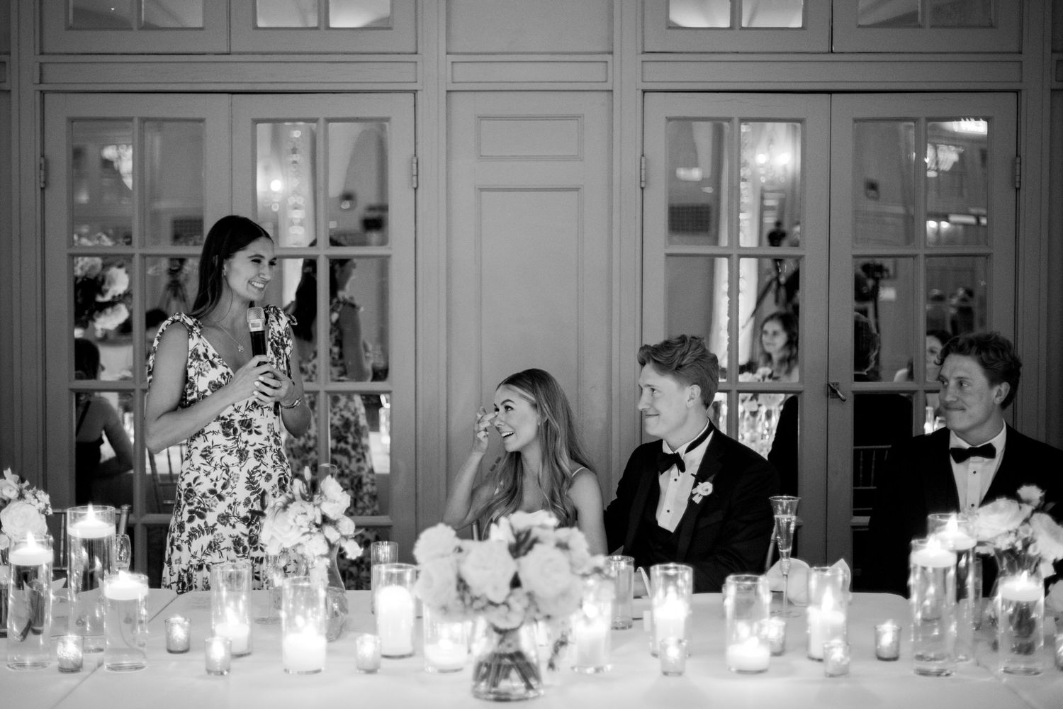 A black and white photo of wedding reception guests enjoying speeches at elegant candlelit dinner table at Hotel President in Kansas City.