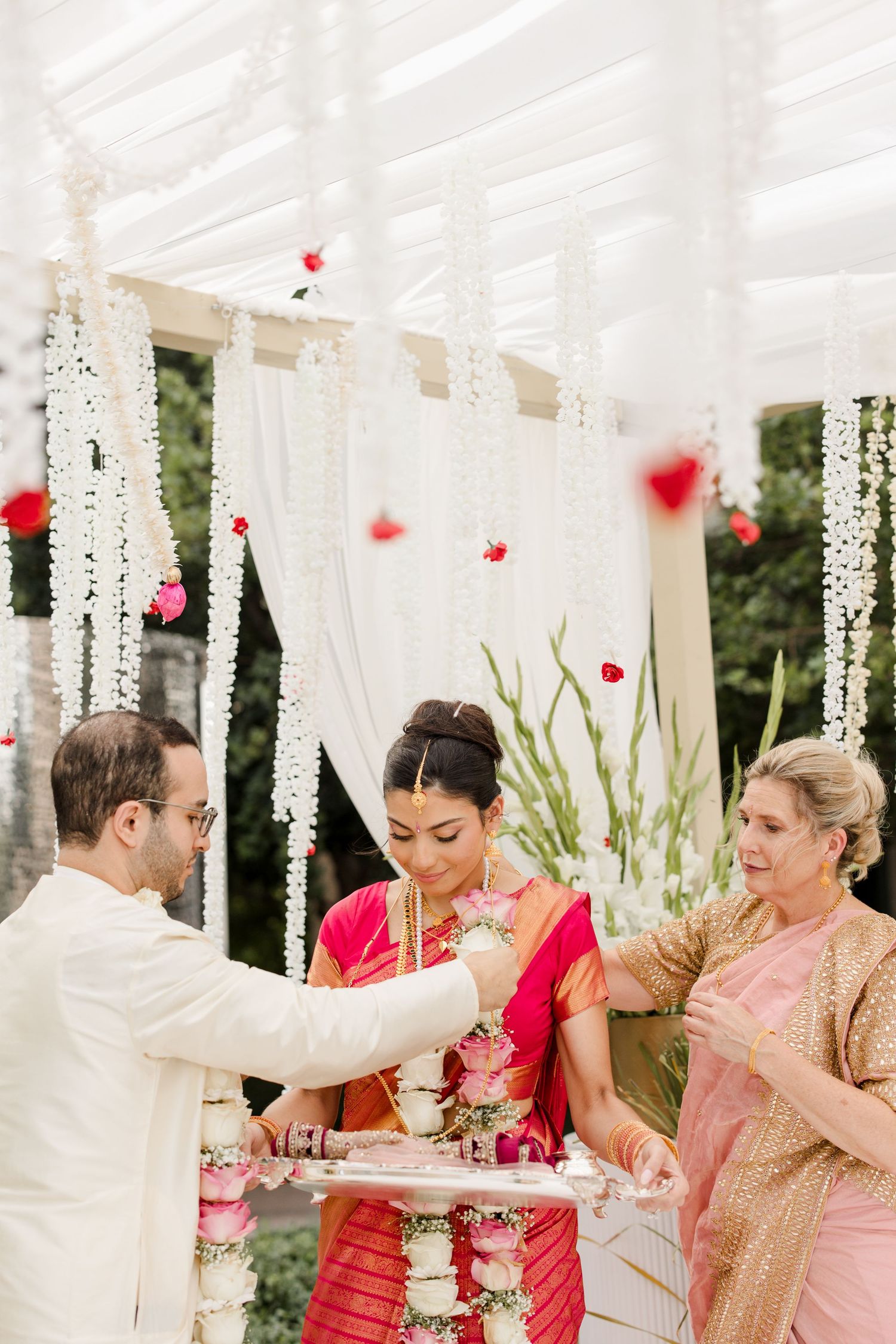 Wedding ceremony under a white draped canopy with red flowers and crystal decorations.