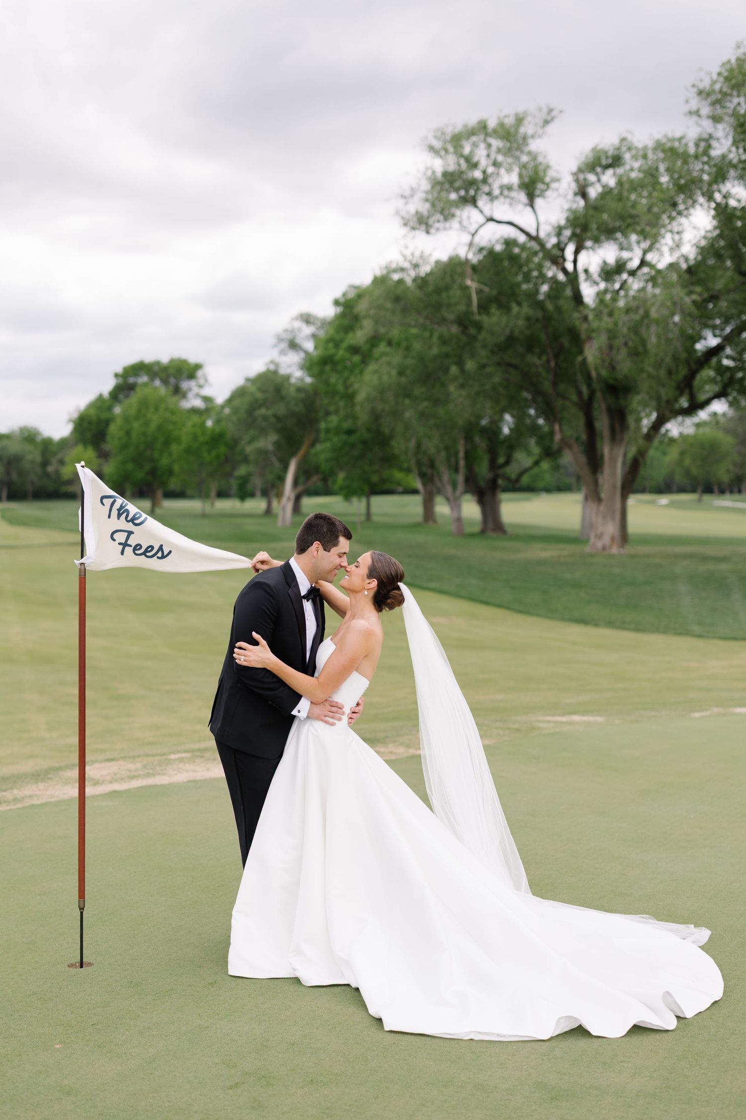 Bride and groom kissing on a golf course beside a custom wedding flag on their wedding day.