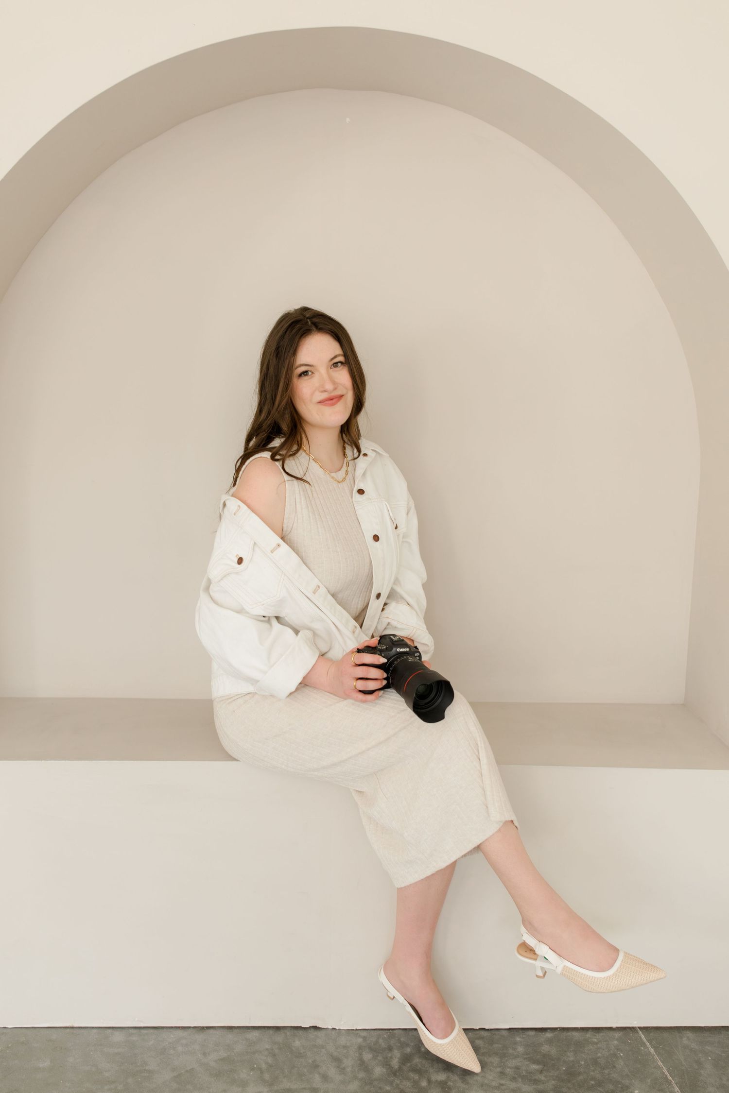 Elegant pose in neutral tones against arched backdrop with camera. Wedding and Portrait Photographer Hannah Rogg Taylor.