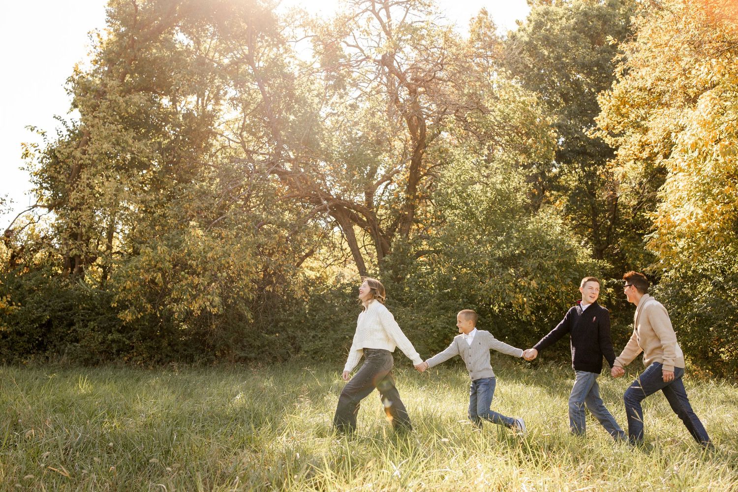 Family playing and running together in a sunlit autumn field at Shawnee Mission Park in Kansas.