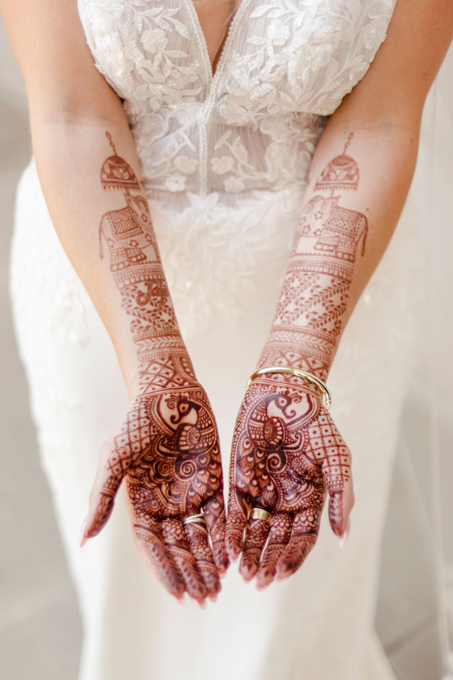 Intricate henna mehndi designs adorning both hands of someone wearing a white wedding dress.