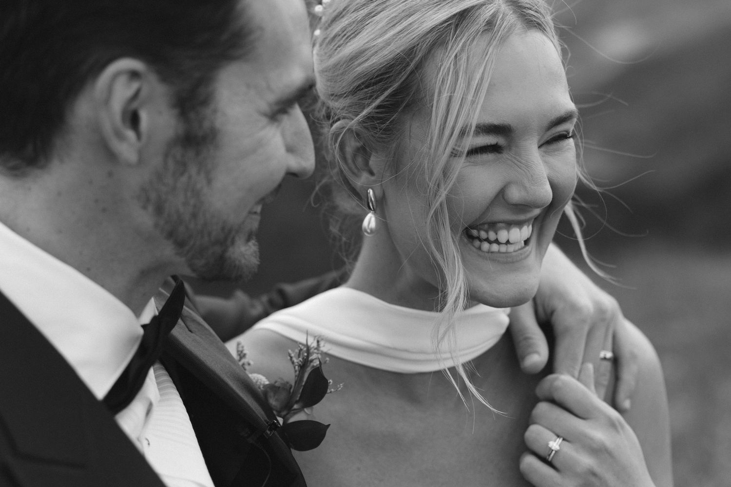 A black and white candid wedding photo showing a joyful moment between a couple with natural outdoor lighting.
