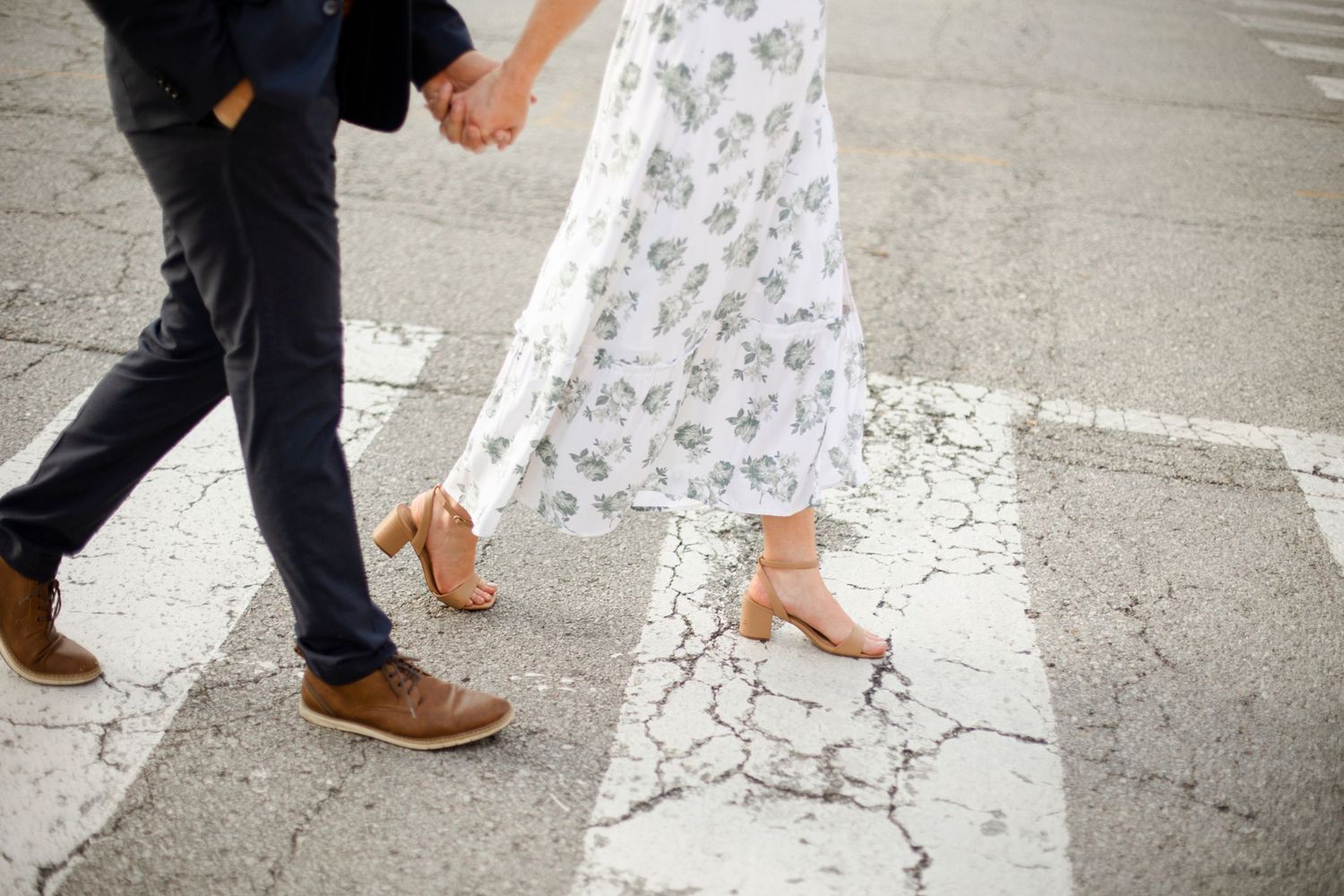 Close-up of couple's feet walking together, showing brown dress shoes and a floral dress hem.