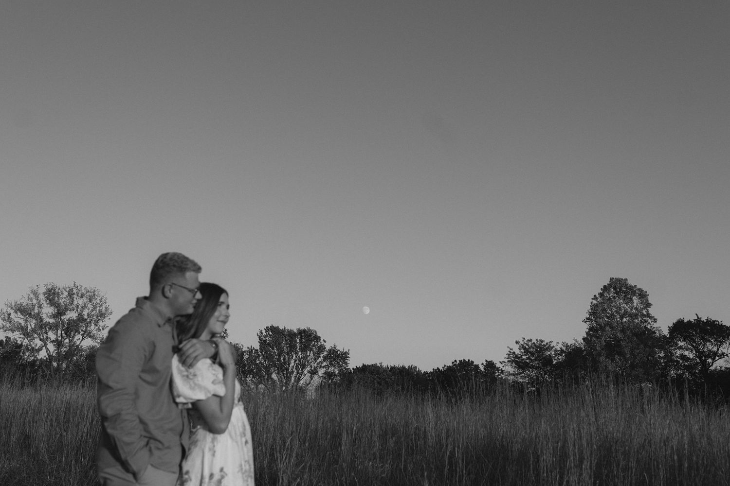Romantic black and white portrait of couple embracing in field at dusk. Wedding photographer Hannah Rogg Taylor