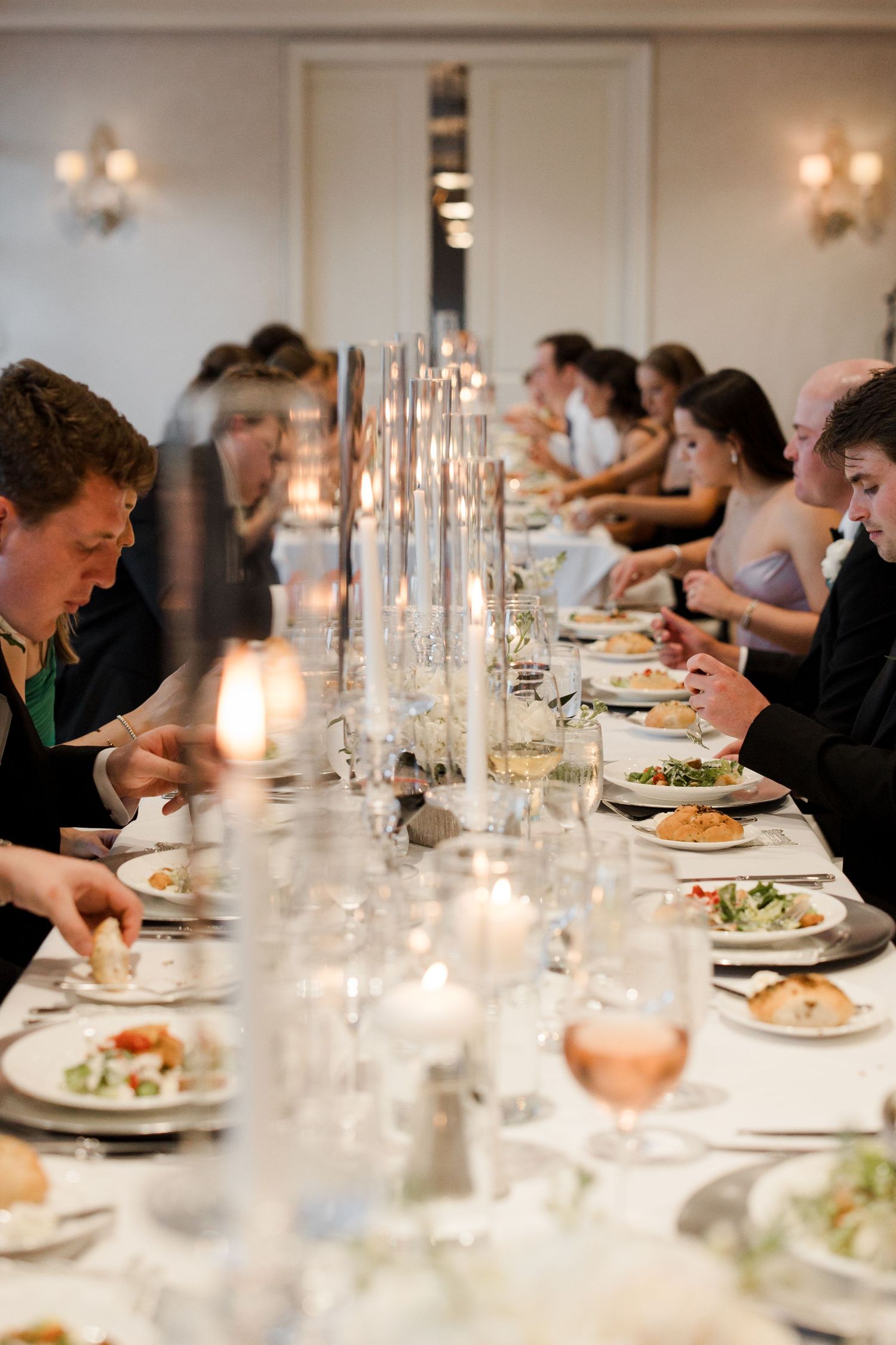 An elegant dinner party table setting with lit candles and glassware stretches across a formal dining room.