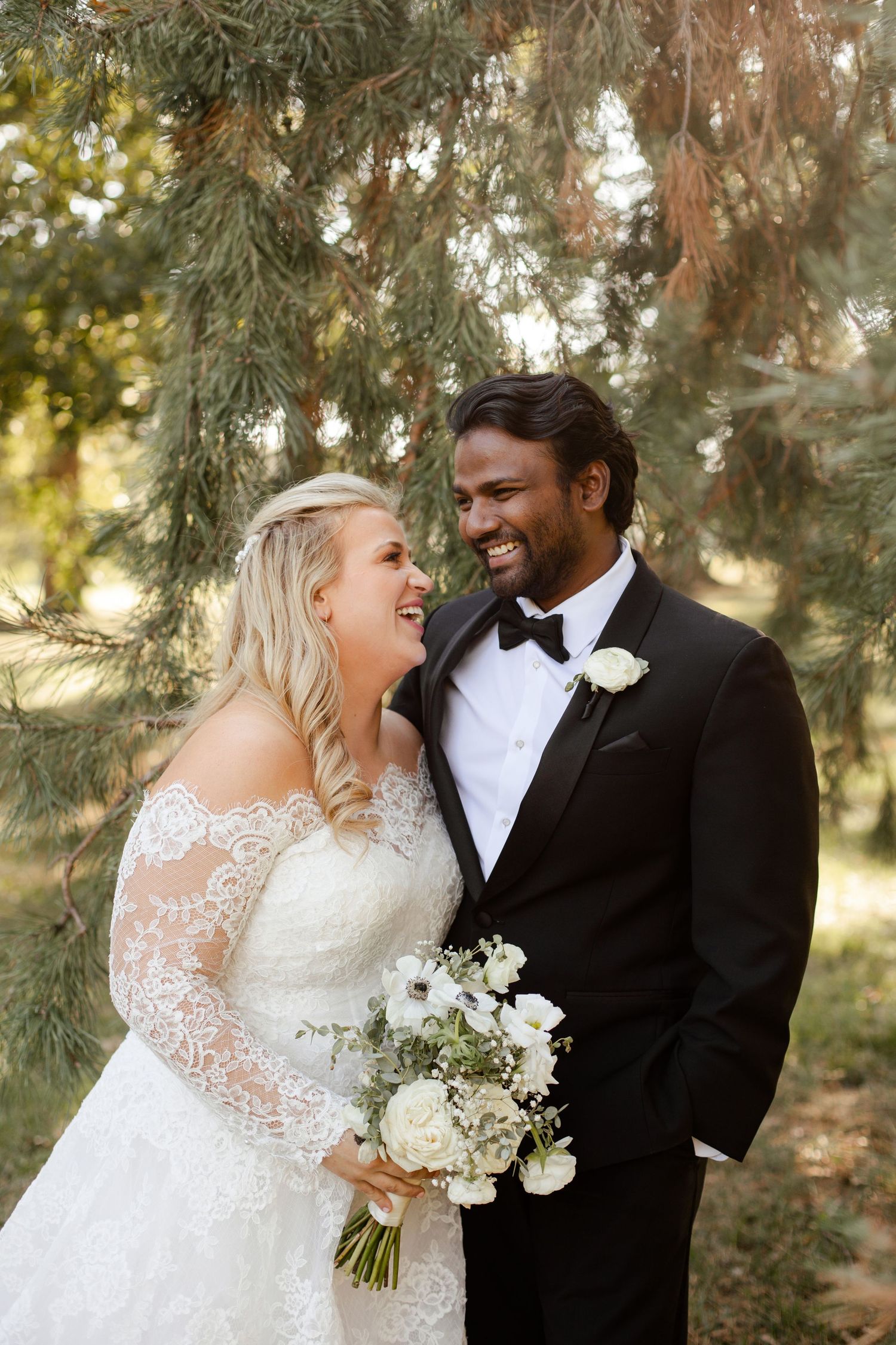 Joyful couple sharing a candid moment under pine trees during their wedding at Loose Park in Kansas City.