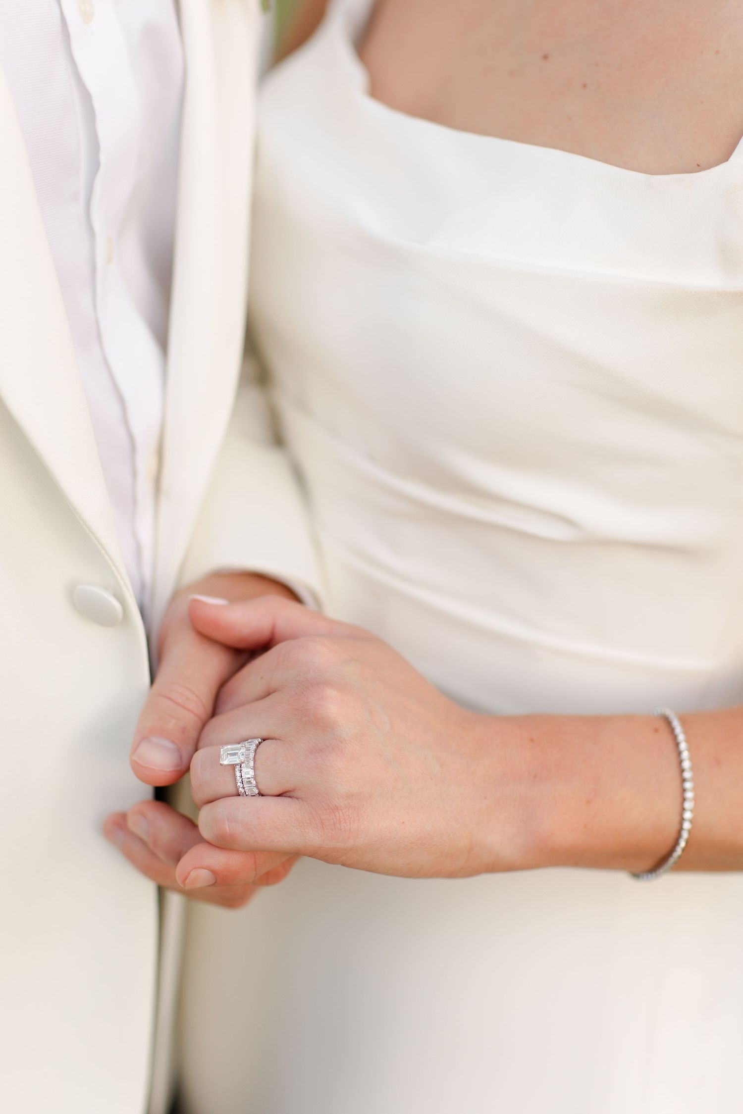 Close-up view of an elegant engagement ring and bracelet on a hand against a white formal dress.