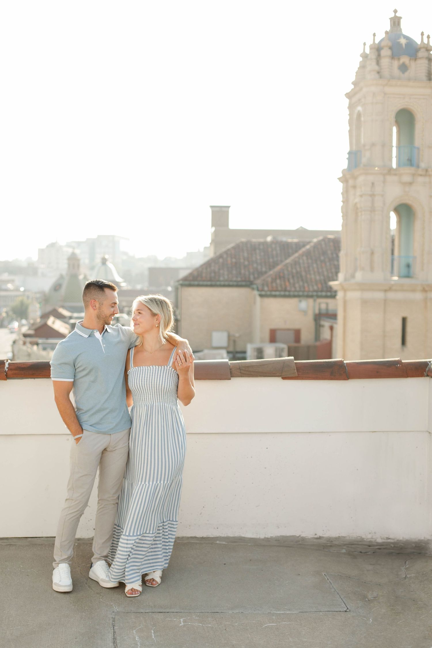 Stylish couple posing on rooftop with historic bell tower and city views at the Kansas City Country Club Plaza.