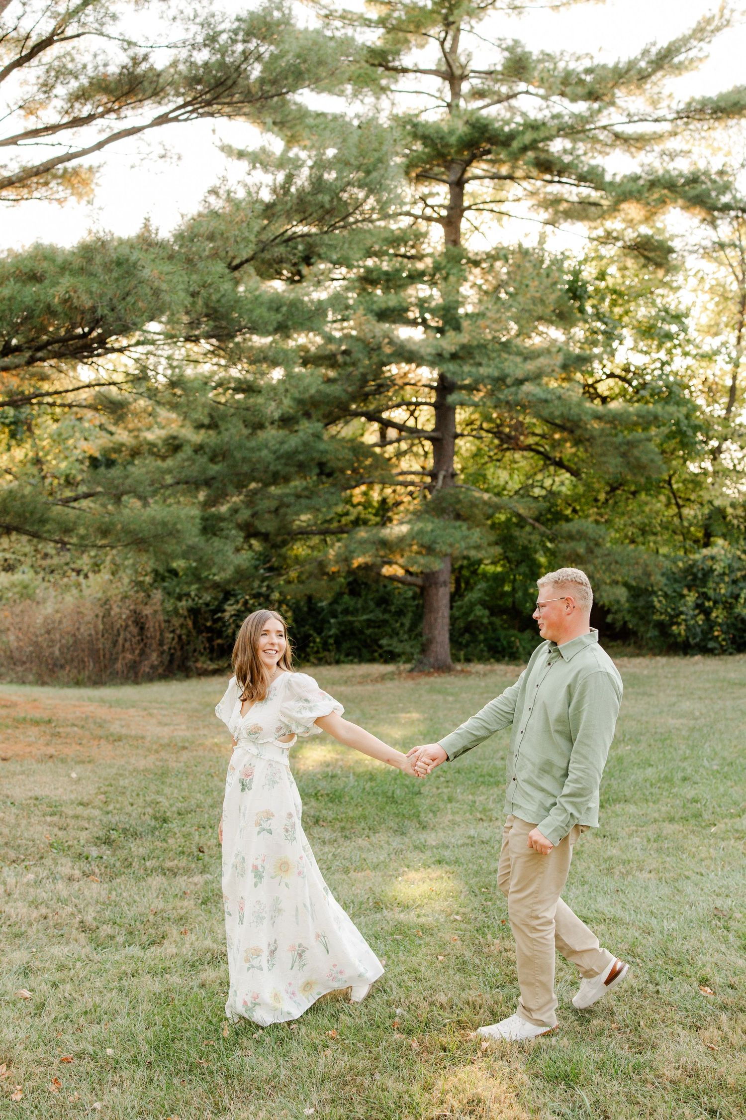 Couple holding hands and dancing in a field with pine trees at sunset, photo by Hannah Rogg Taylor