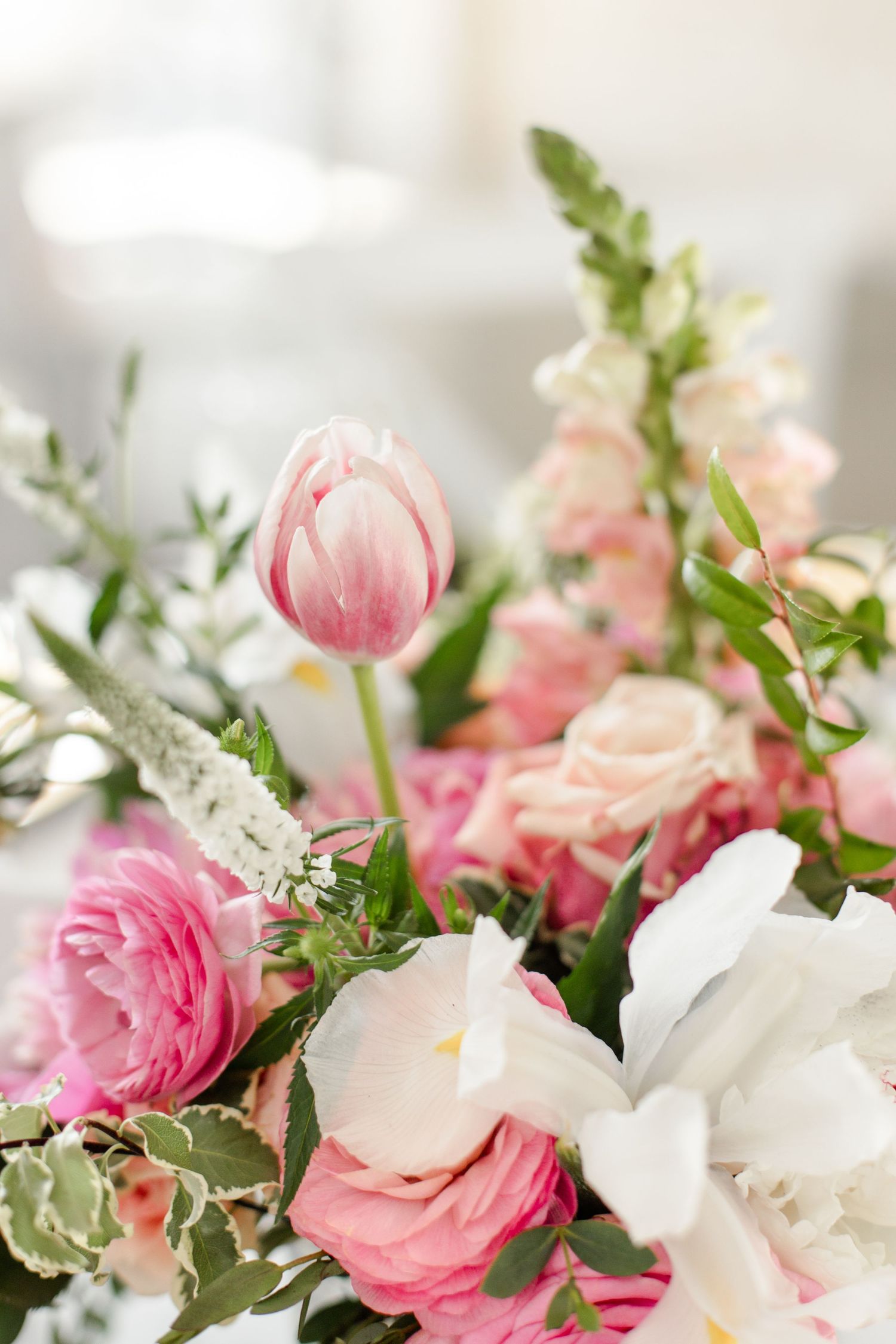 A delicate floral arrangement featuring pink tulips, roses, and white blooms with soft greenery.