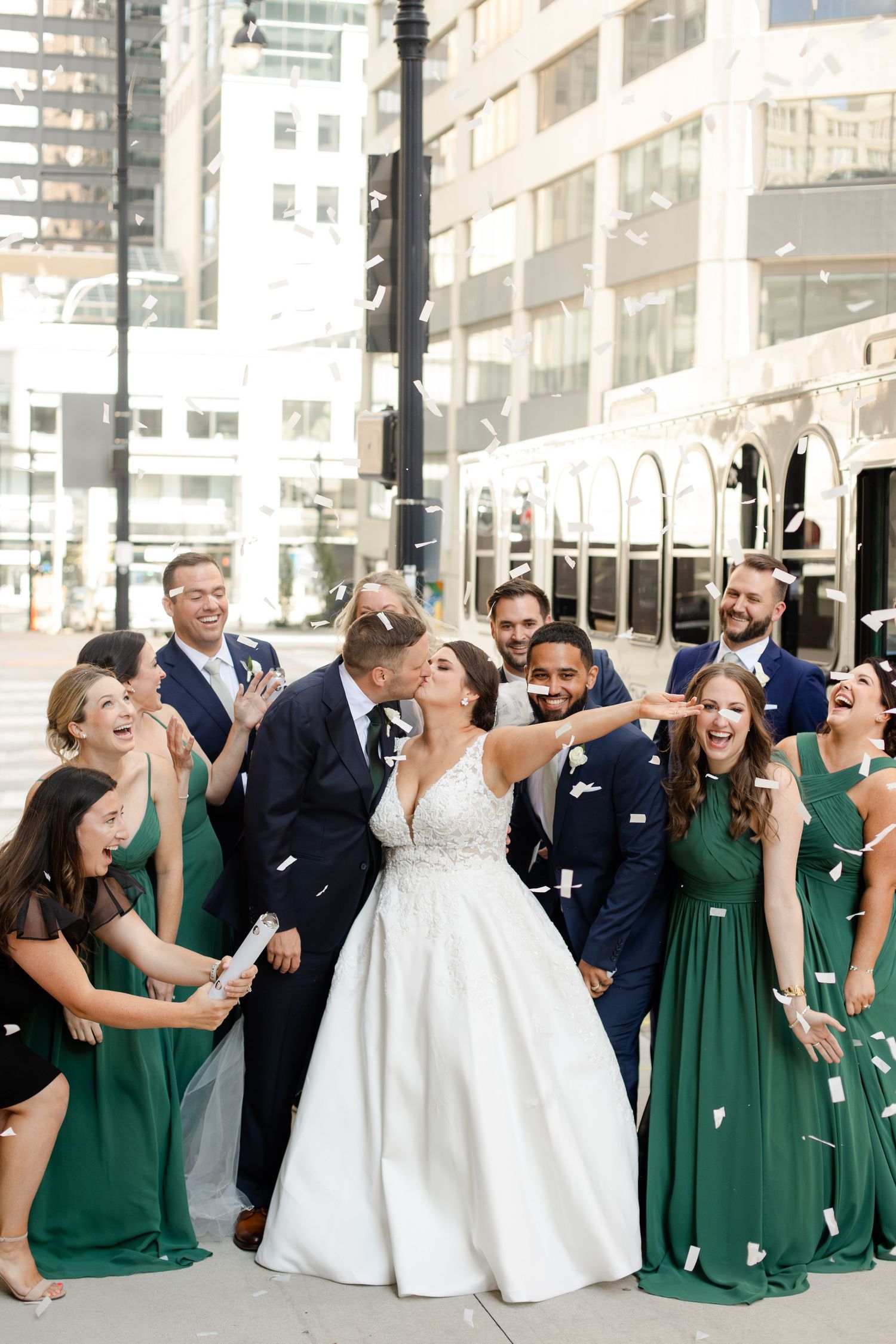 Wedding party celebrates on city street with bridesmaids in emerald green dresses. Kansas City Wedding Photography by Hannah Taylor.