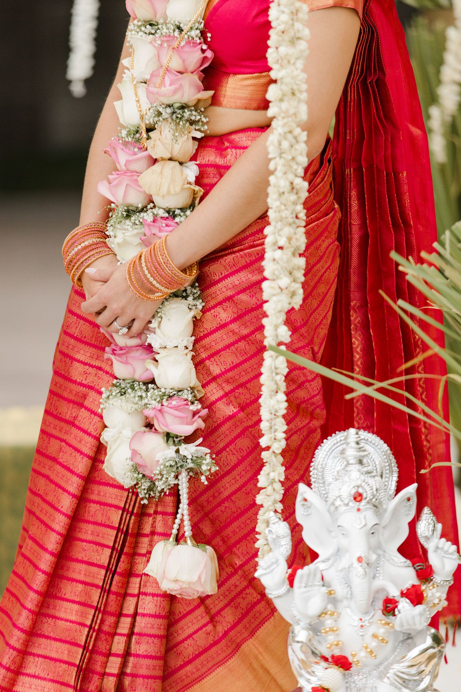 Close-up view of red bridal saree pleats adorned with intricate white floral garlands and traditional silver decor pieces.