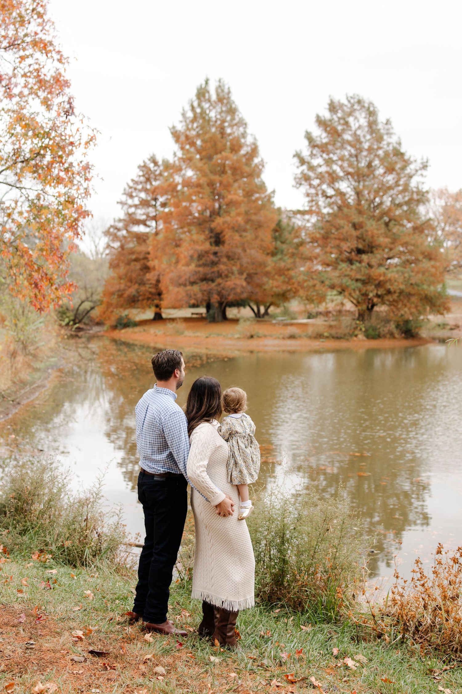 Family standing by a serene autumn lake with golden trees in the background.